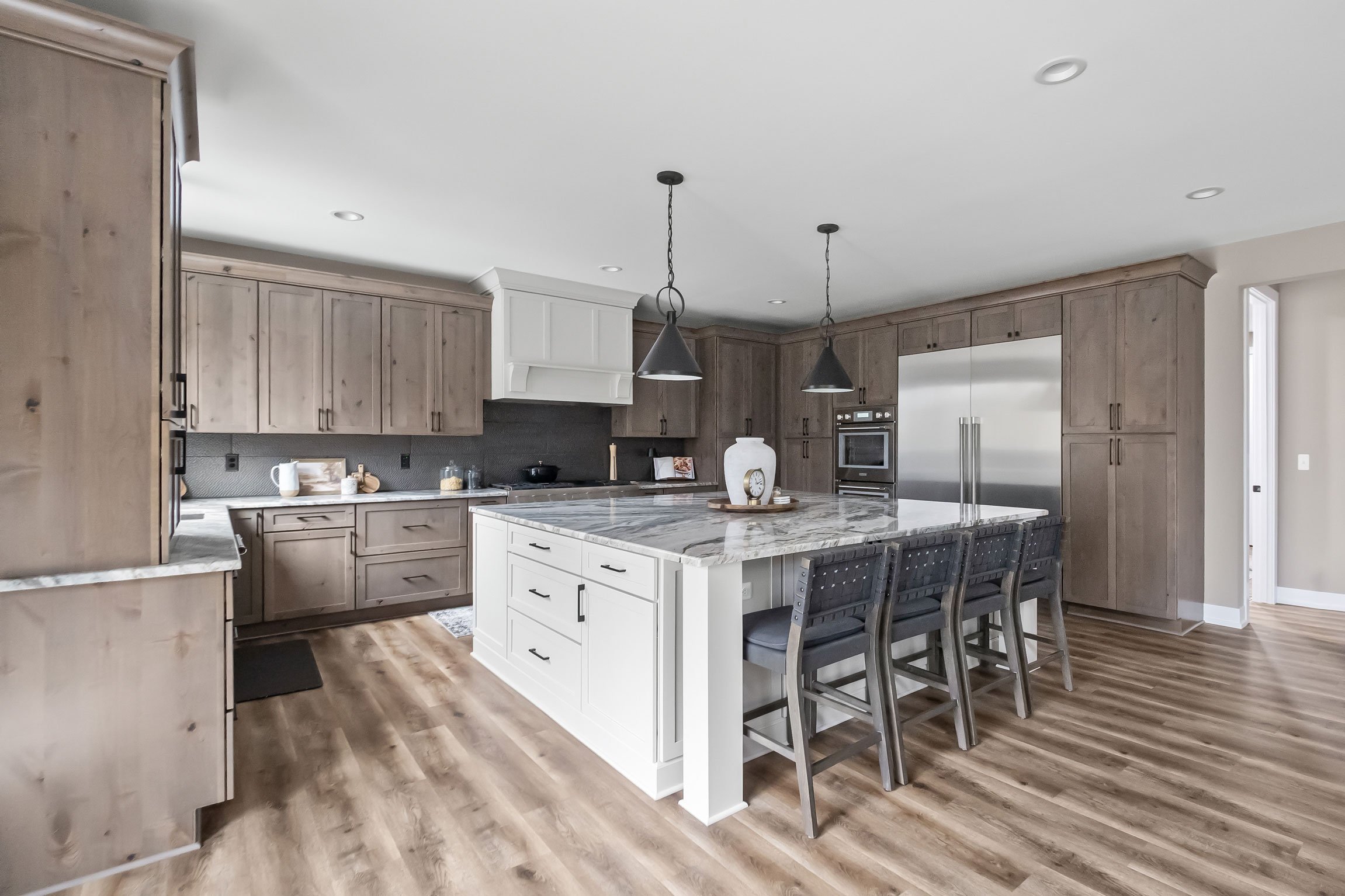 Open-concept kitchen featuring Rustic Alder perimeter cabinetry, a large white island with Fantasy Brown granite countertops, and mixed metal pendant lighting.