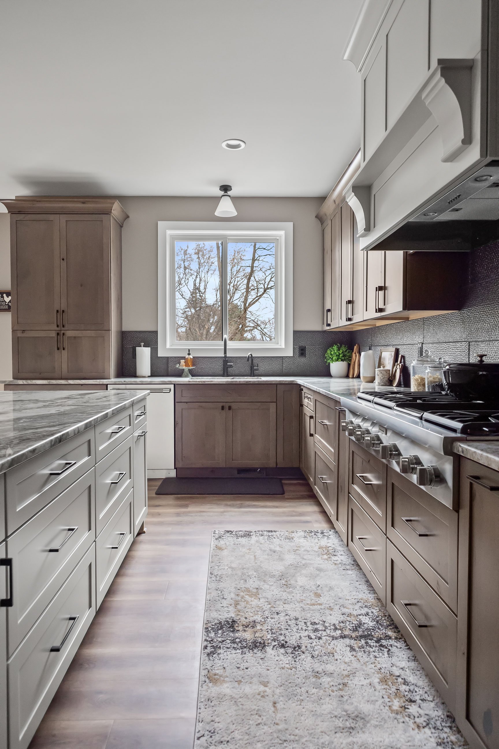 L-shaped kitchen layout with Rustic Alder cabinetry, matte black faucet, Fantasy Brown countertops, and natural light from a large window.