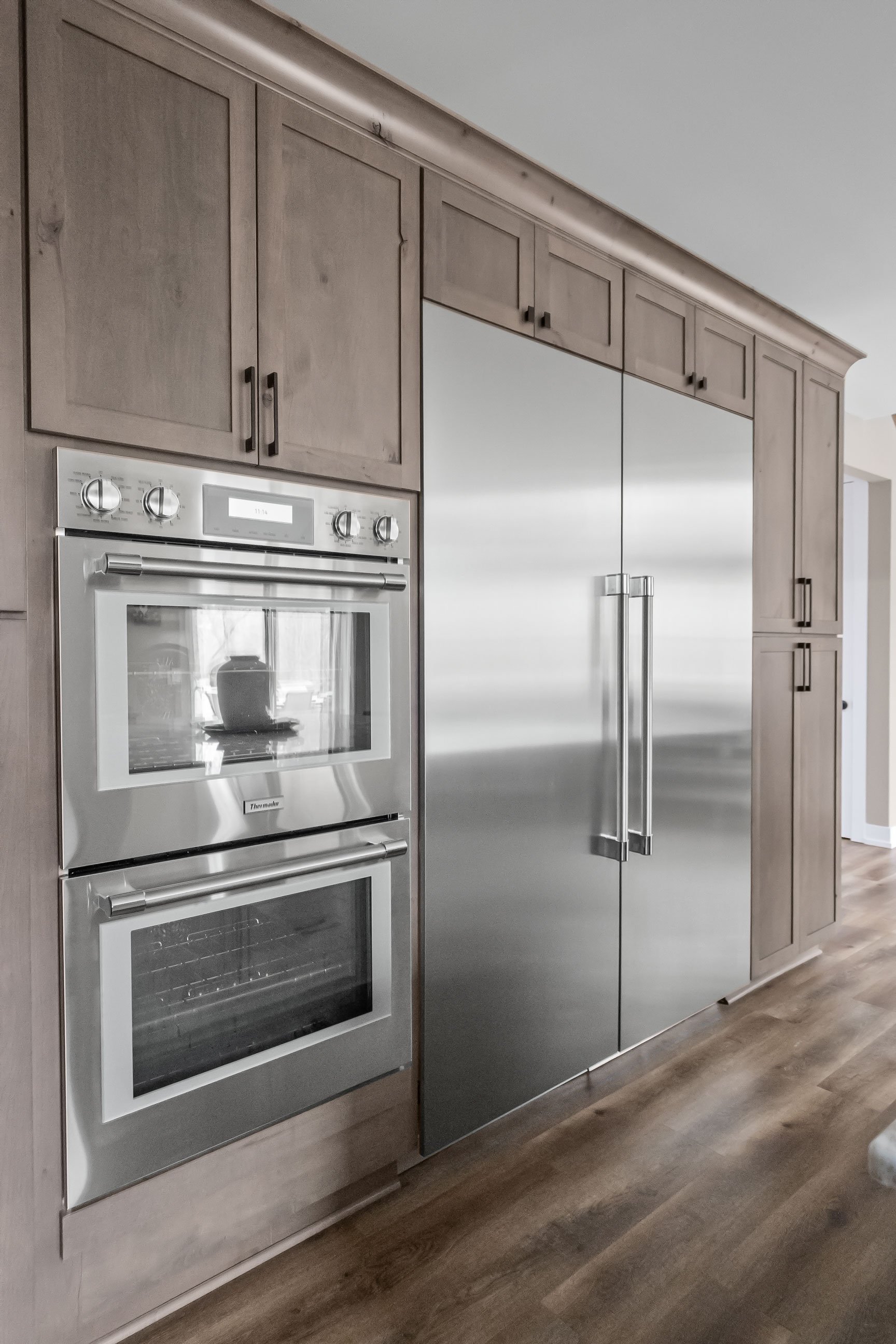 Rustic Alder tall cabinetry housing stainless steel double ovens and a large built-in refrigerator, creating a seamless wall of storage.