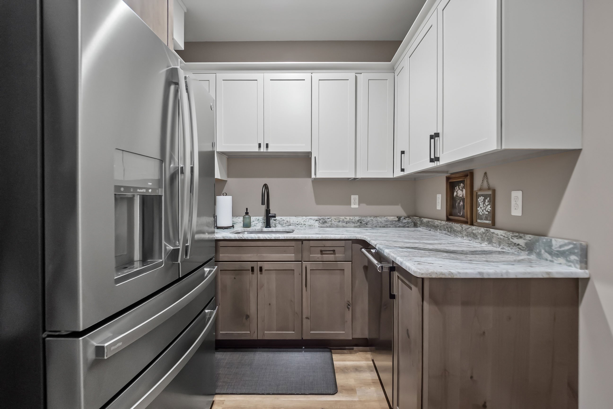 Walk-through pantry featuring mixed white upper cabinets and Rustic Alder base cabinets with ample counter space and stainless steel refrigerator.
