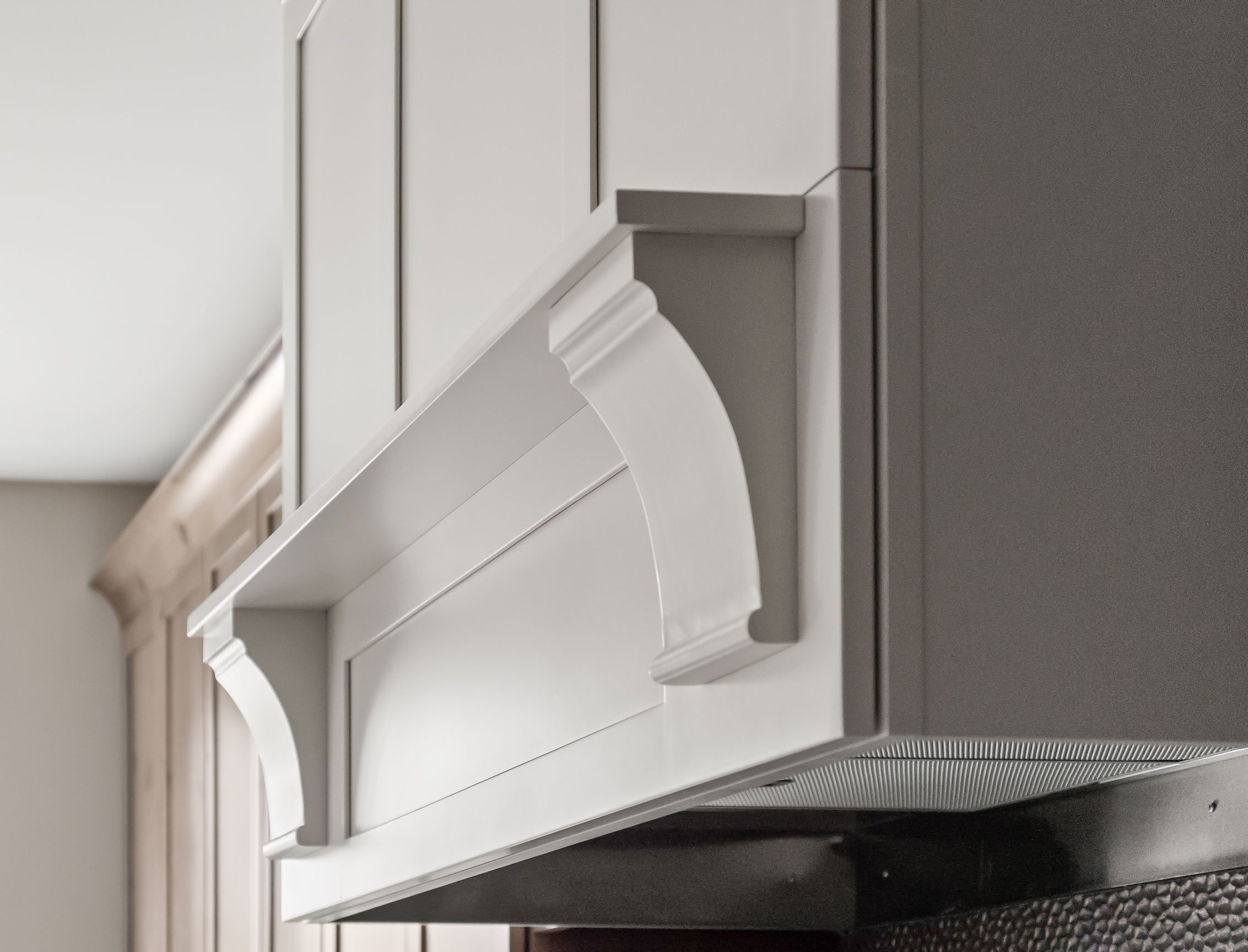 Soft white range hood with decorative corbels, contrasting with Rustic Alder cabinetry.