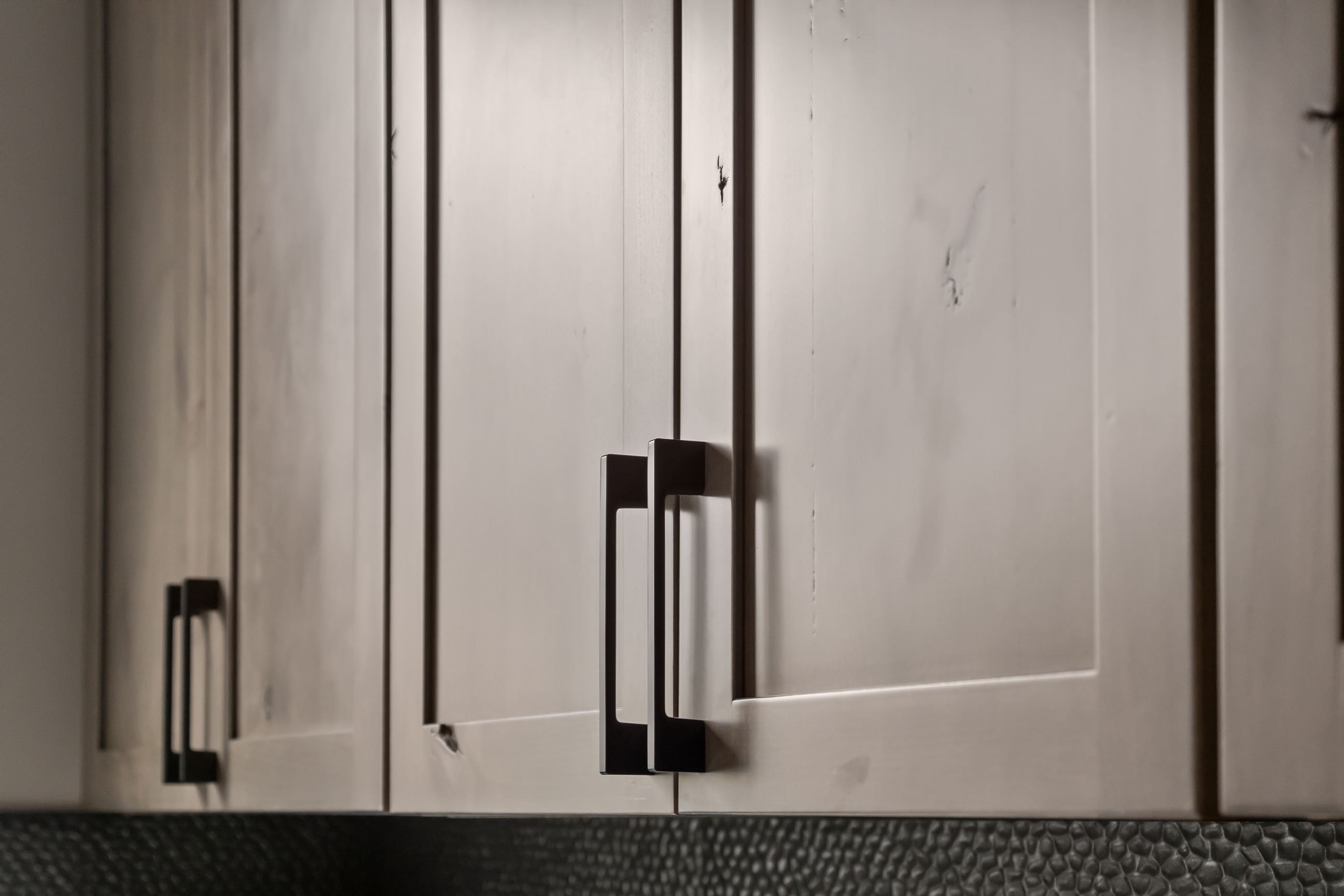 Close-up of Rustic Alder Shaker cabinet doors highlighting natural knots, dark stain, and modern black hardware.