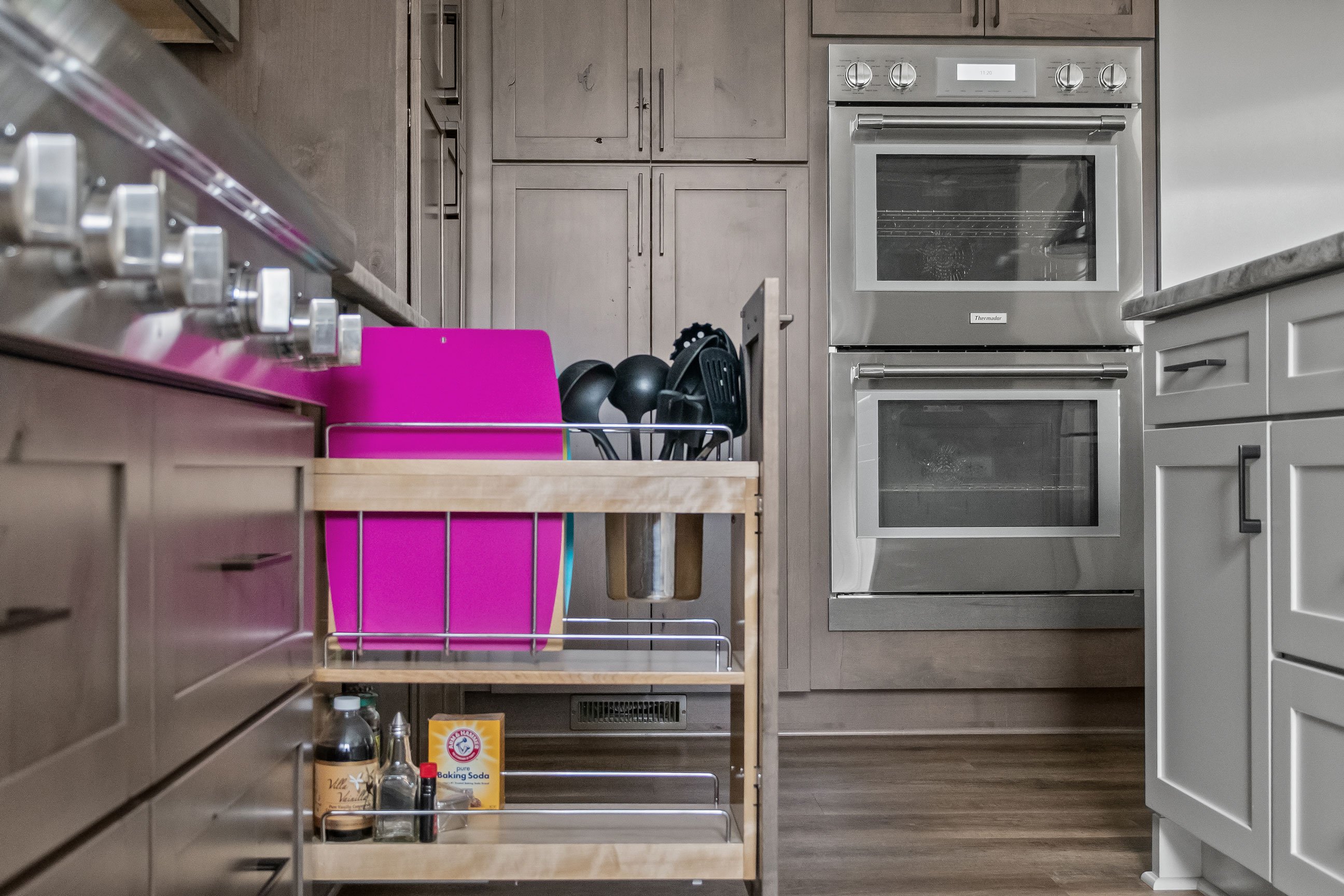 Pullout cabinet organizer holding utensils and baking items, located beside the stainless steel range top.
