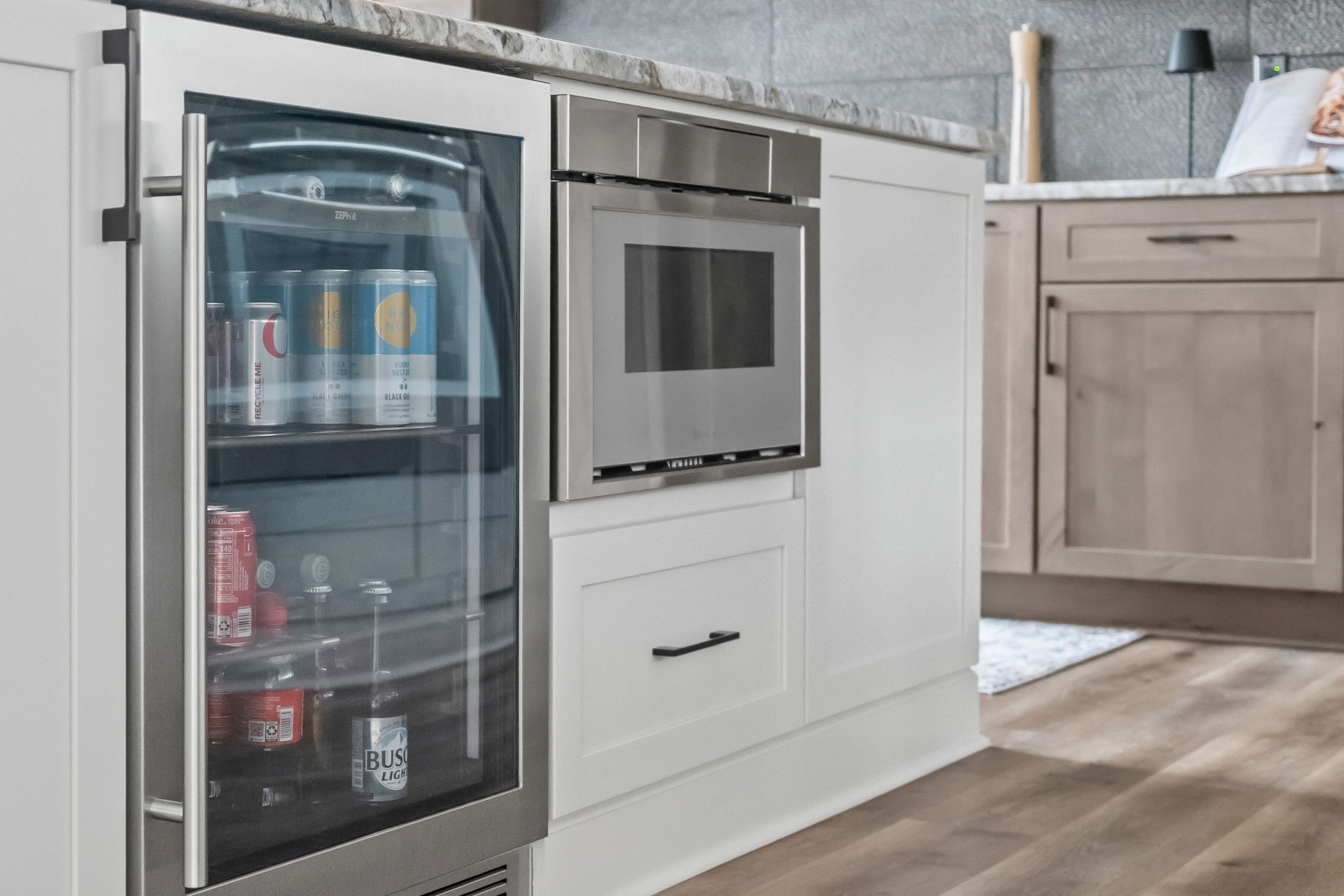 Beverage cooler and built-in microwave integrated into the white kitchen island, with stainless steel accents and granite countertop.