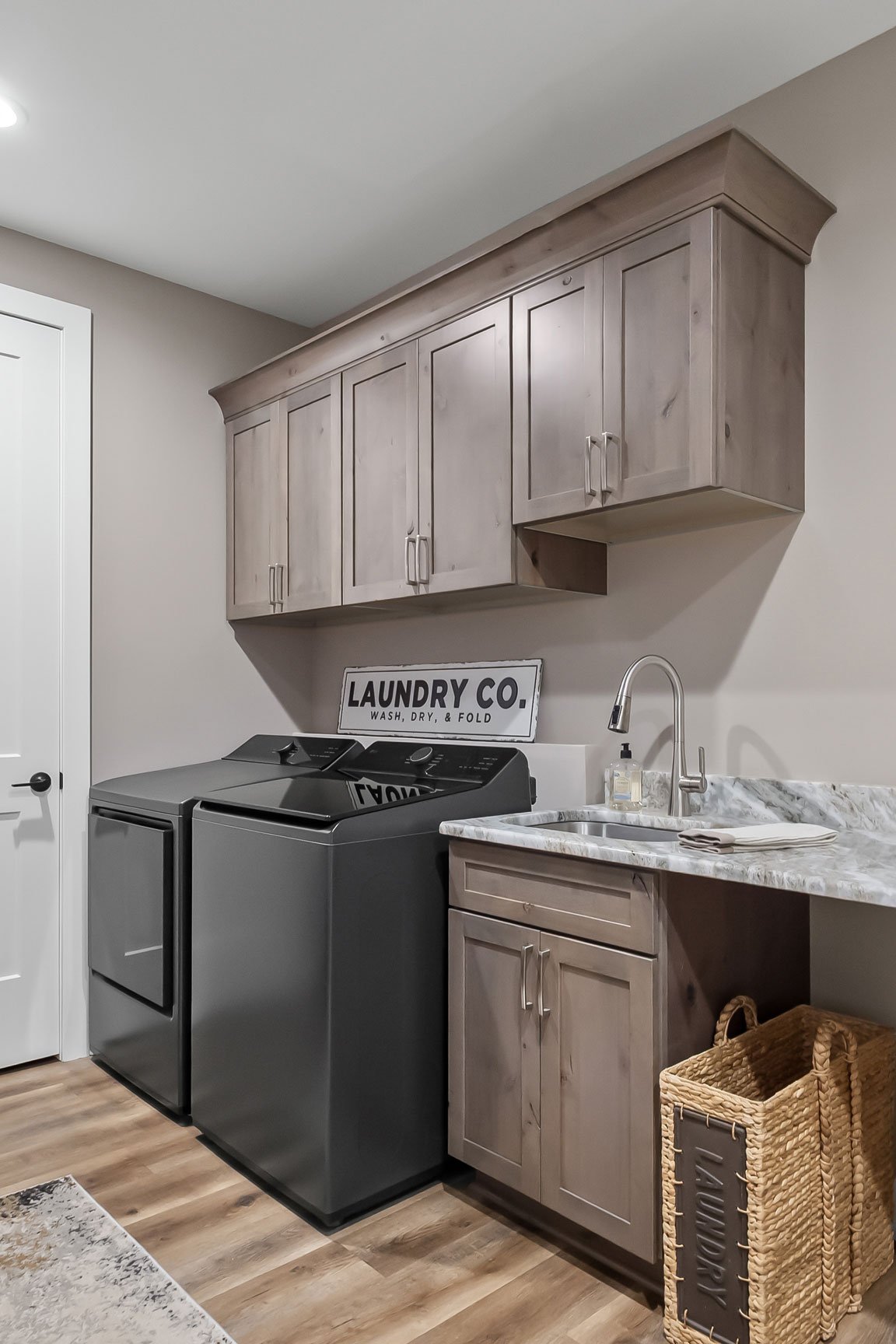Laundry room design with Rustic Alder cabinets, dark appliances, utility sink, and ample folding space on Fantasy Brown countertops.