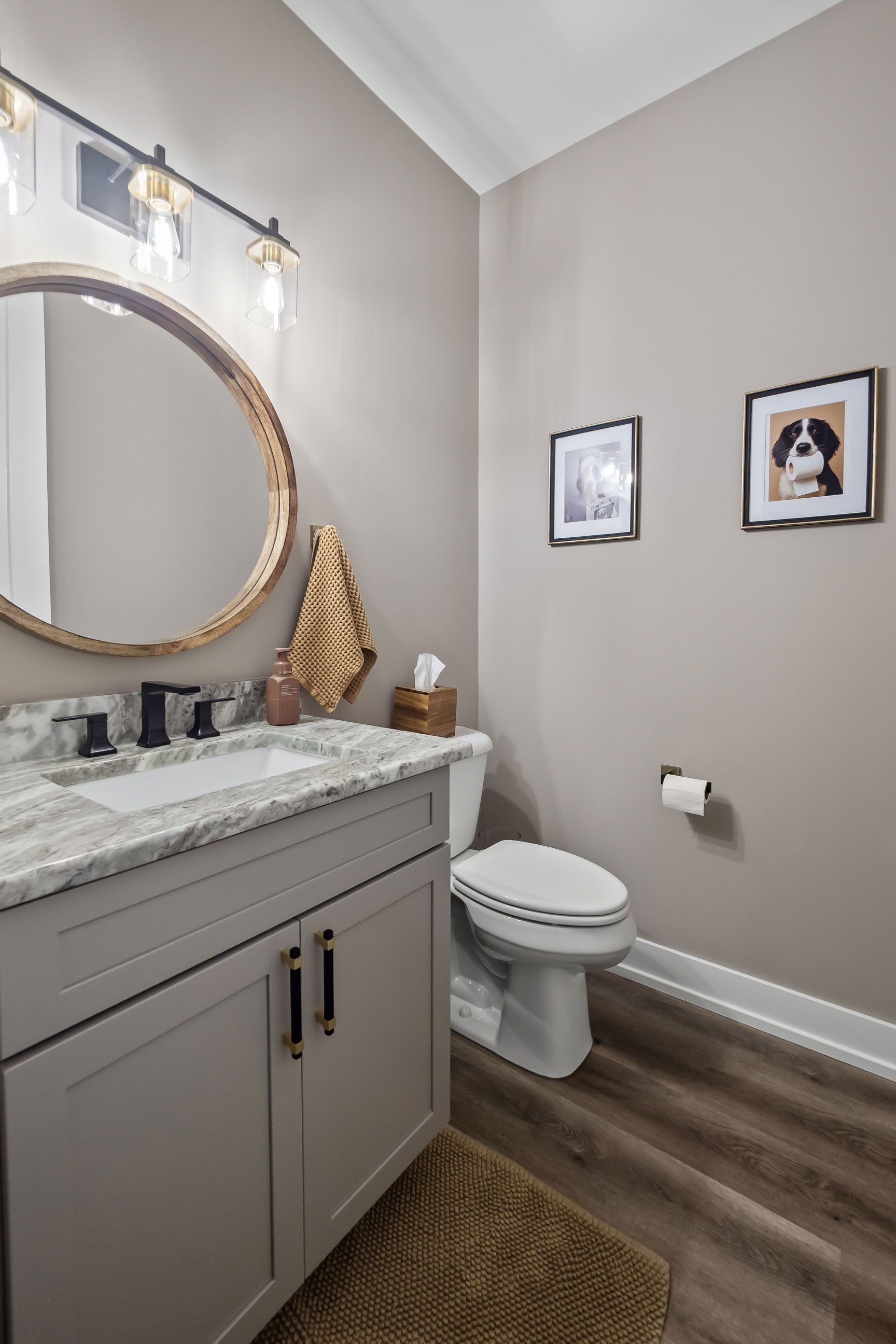 Powder room featuring a gray Shaker vanity, matte black faucet, and round wood-framed mirror with modern lighting.