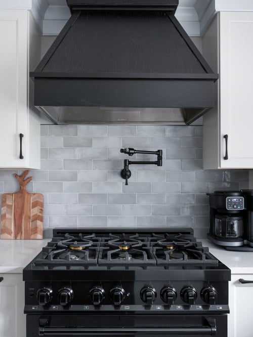 Medallion Cabinetry hood in Oak with Carriage Black paint; cabinetry in Wallace door style in Sea Salt White paint, Marazzi Rice Grey tile