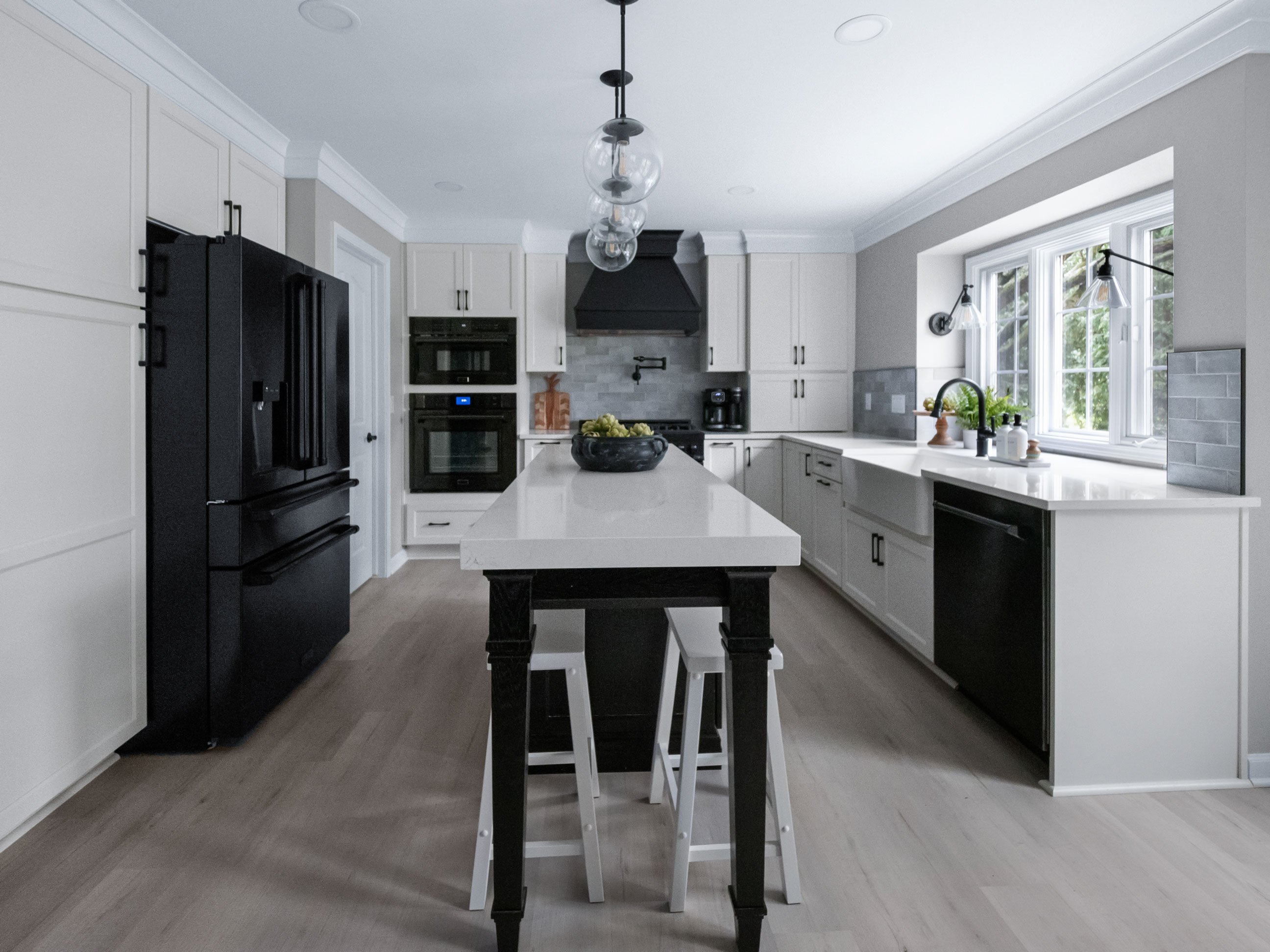 Medallion Cabinetry Wallace door style; island in Oak with Carriage Black paint; perimeter in Sea Salt White paint