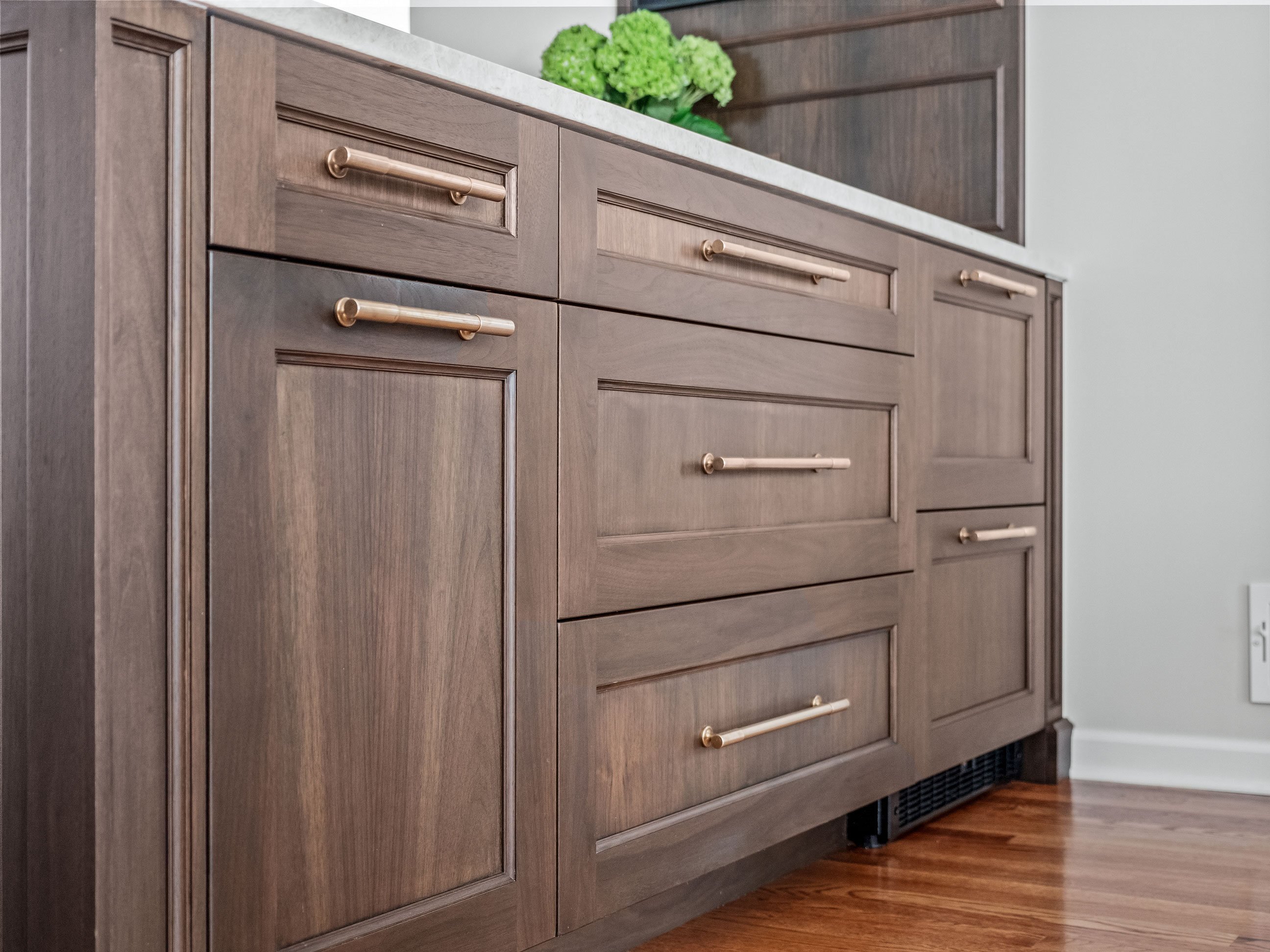 Kitchen with cabinetry in warm white and walnut finishes, antique brass hardware, and warm stone tops