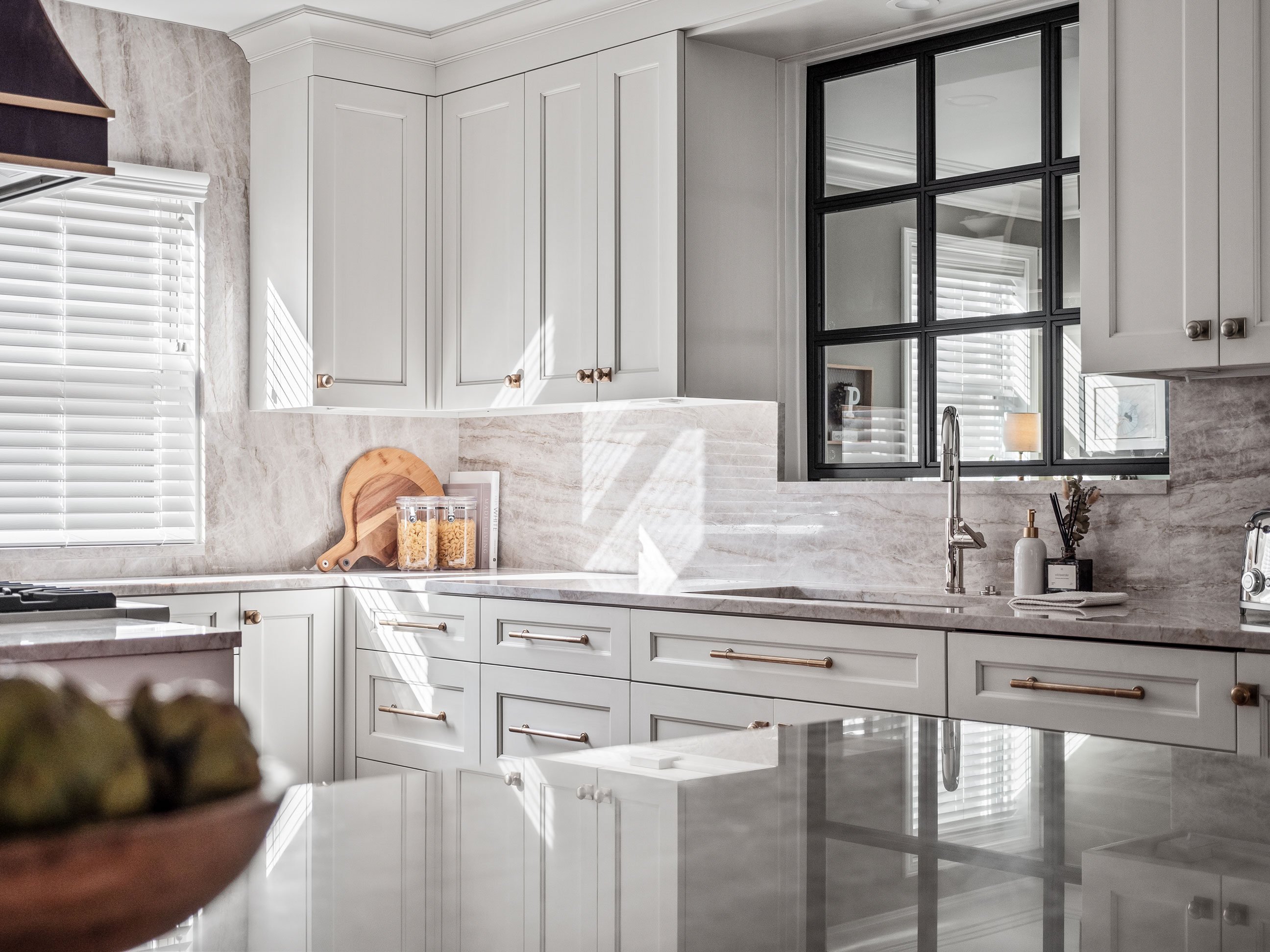 Kitchen with cabinetry in warm white and walnut finishes, antique brass hardware, and warm stone tops