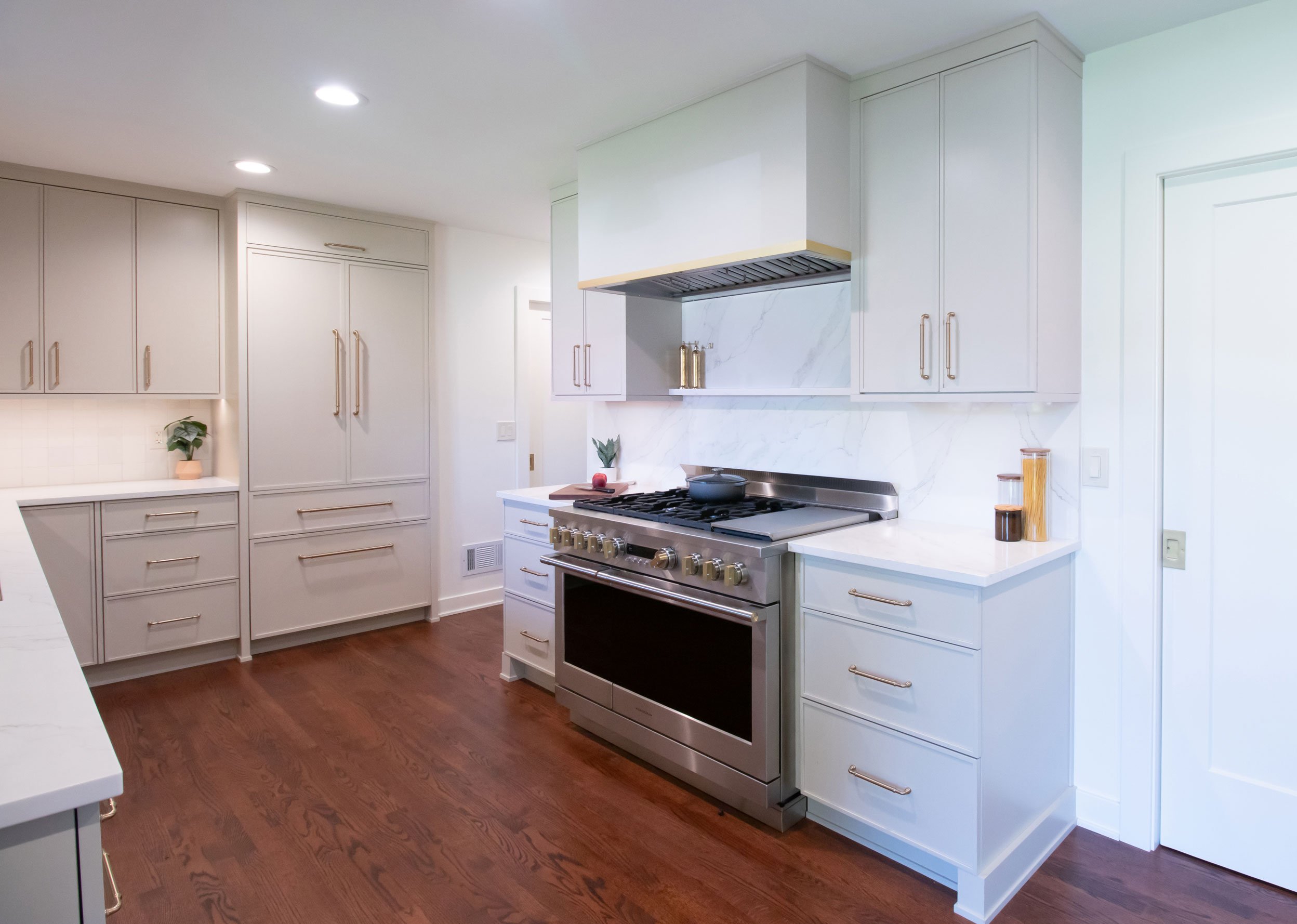 Inspira Cabinetry in the Aspen door style with Accessible Beige finish, custom hood, brushed gold accents, Monogram range