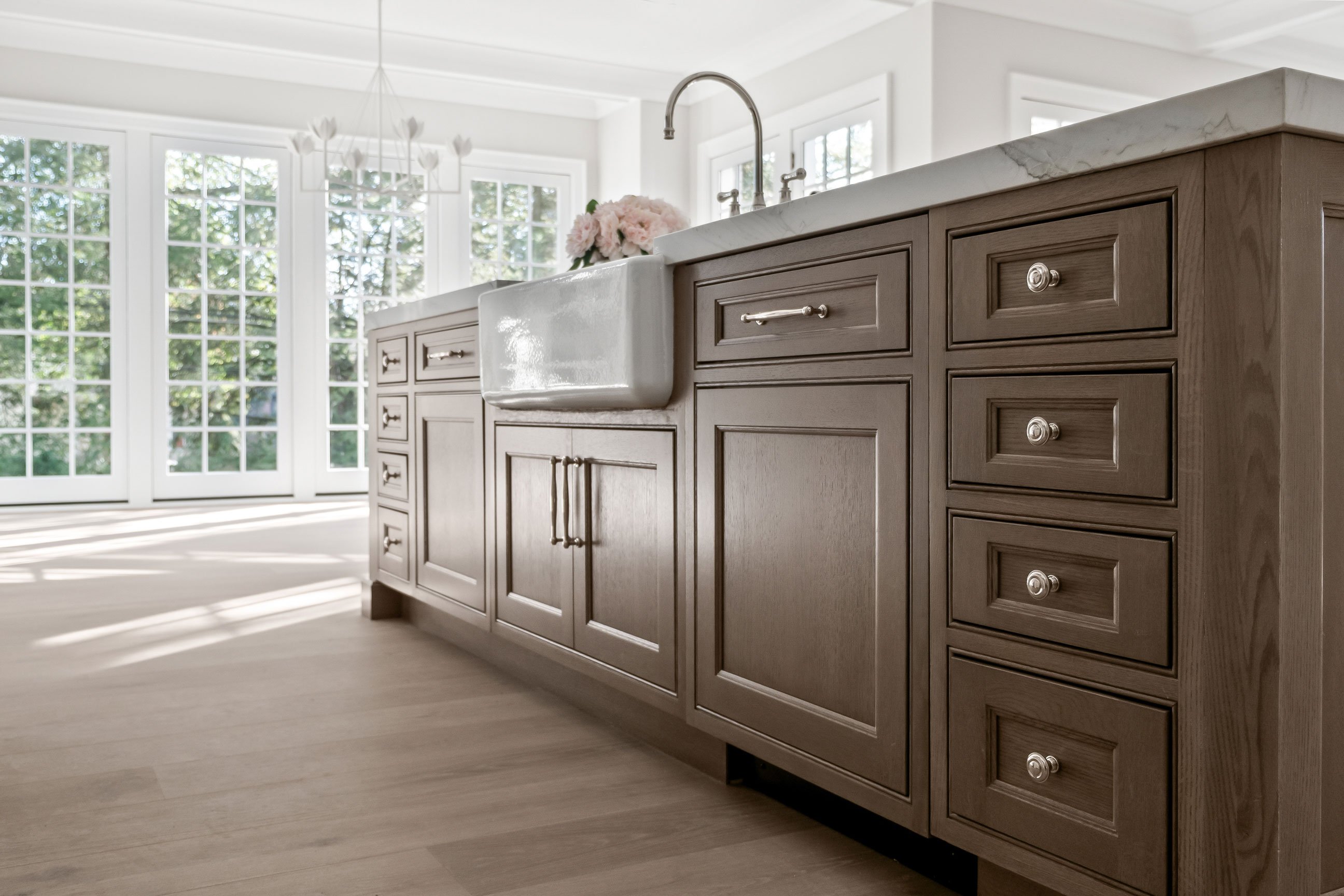 Elegant kitchen view featuring marble backsplash, farmhouse sink, and warm wood island cabinetry designed by KSI.