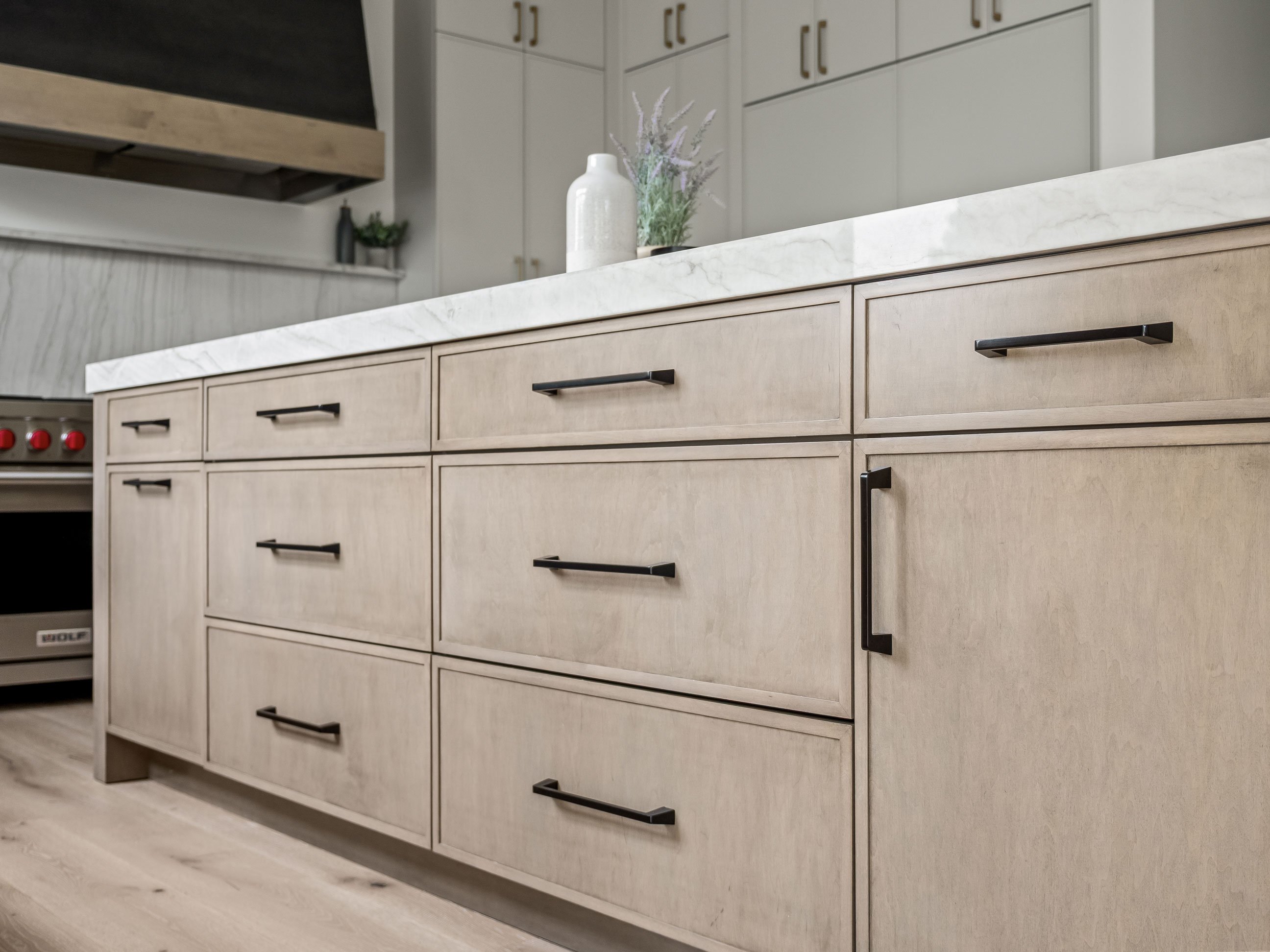 Kitchen island featuring warm wood cabinetry with statement hood in background