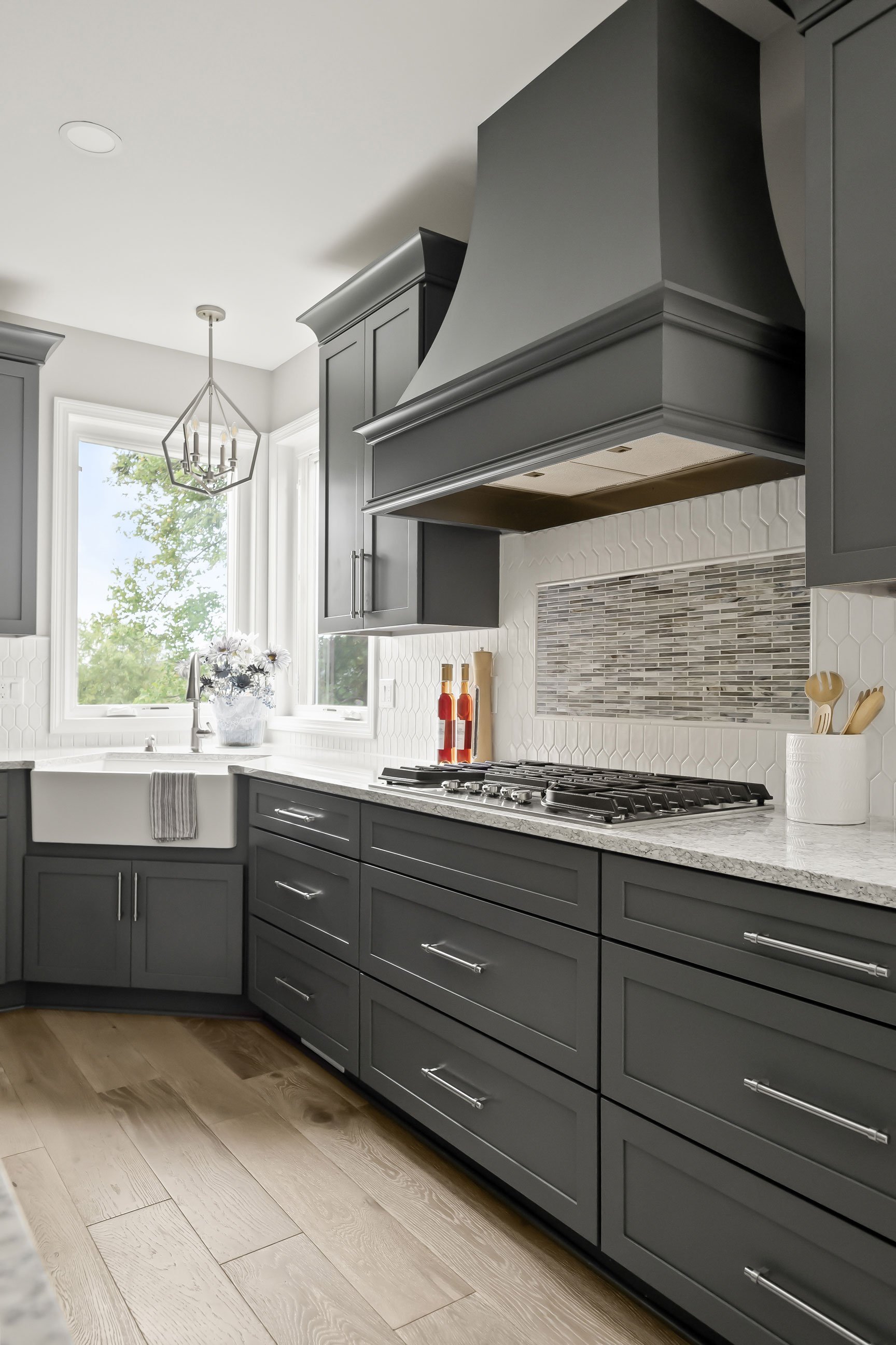 Decorative range hood and cooktop with gray shaker cabinets, white hex backsplash, and mosaic accent tile creating a stylish focal point.