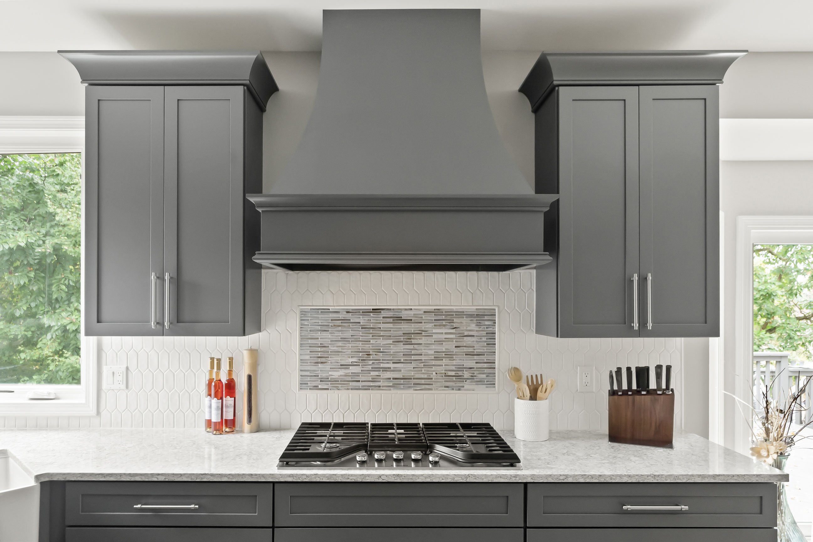 Decorative range hood and cooktop with gray shaker cabinets, white hex backsplash, and mosaic accent tile creating a stylish focal point.