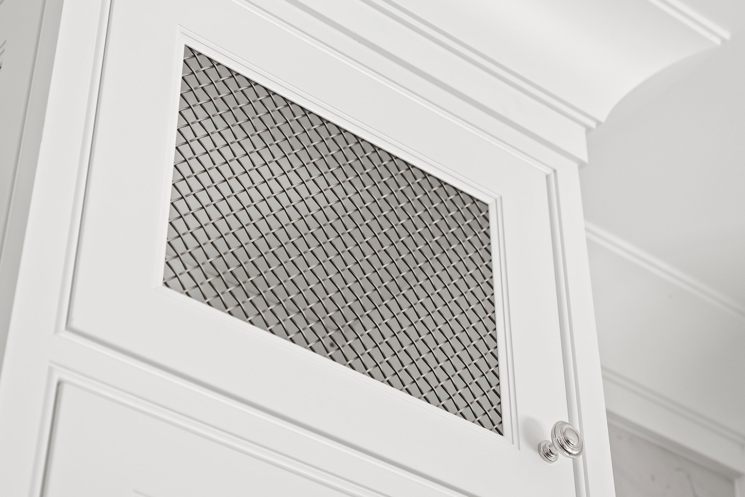 Mesh insert detail in cabinetry tower flanking the hood in the kitchen.