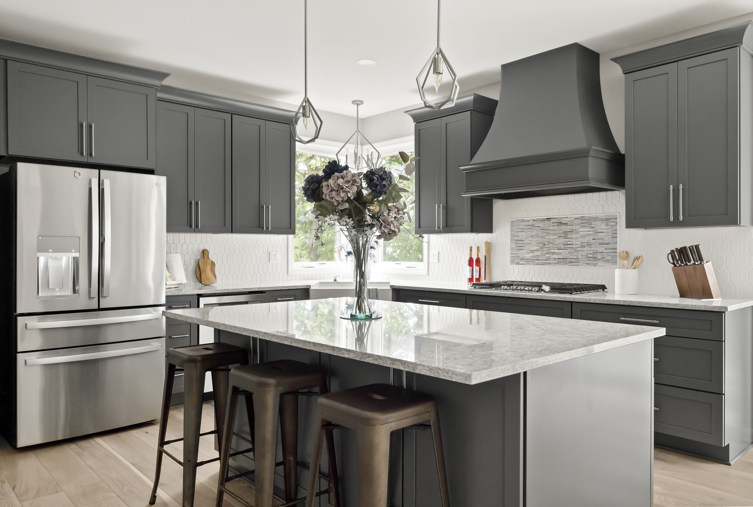 Bright transitional kitchen featuring a bold gray hood, white countertops, and a spacious island with seating for four.