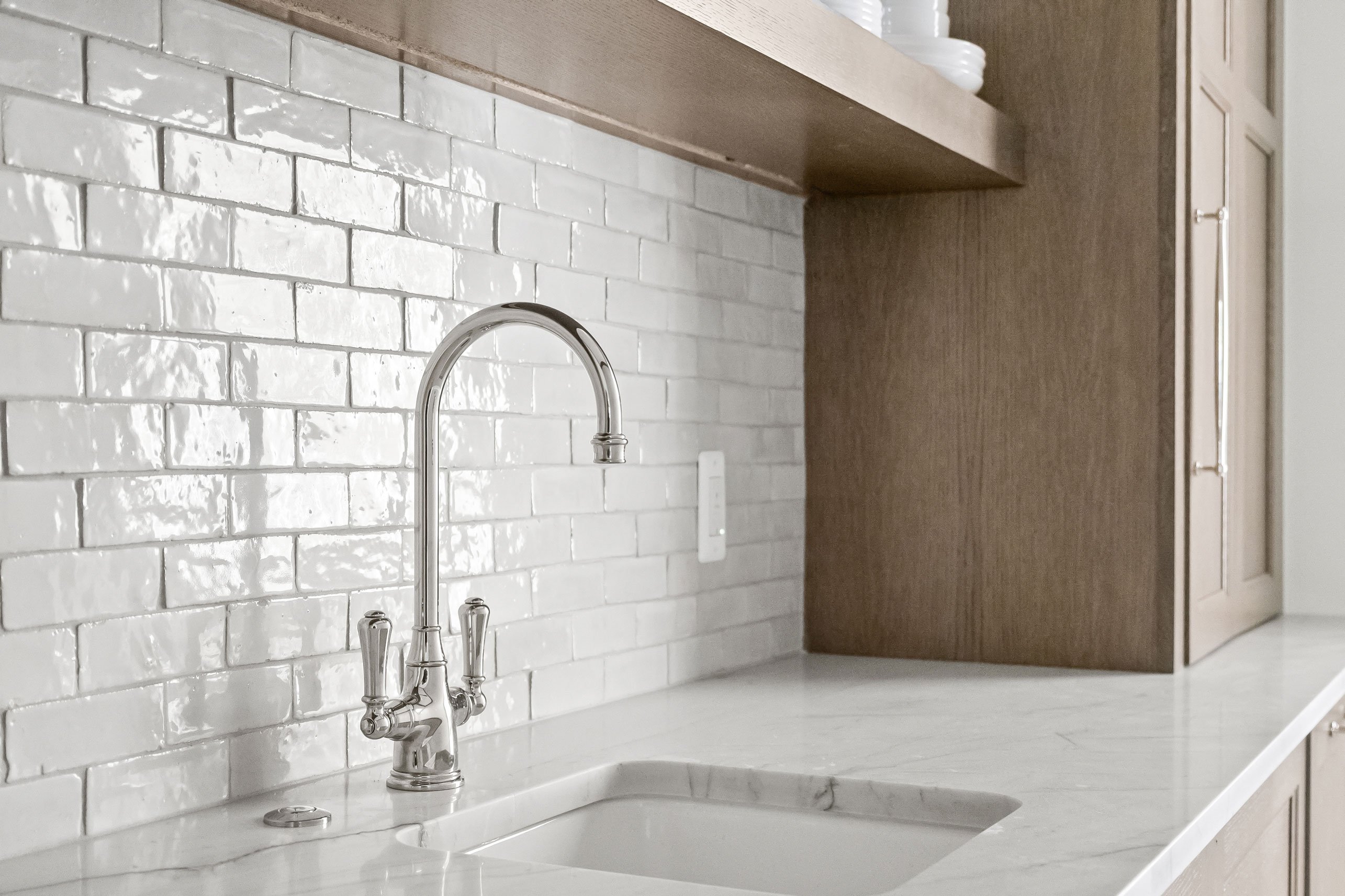 Sink detail in butler's pantry featuring warm white oak cabinetry and white tile backsplash.
