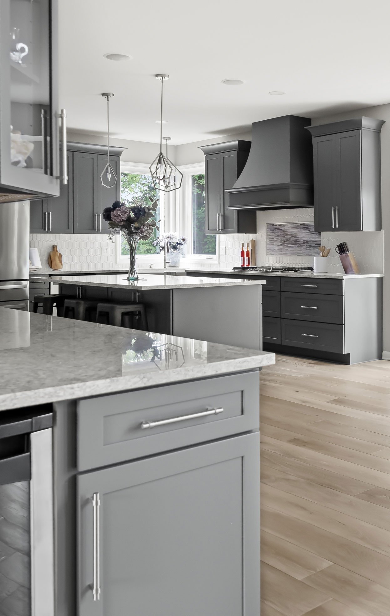 View from coffee bar, showcasing expansive modern kitchen with gray shaker cabinets, stainless steel appliances, and light wood floors creating an airy open layout.