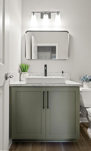 Powder room with sage green vanity, white quartz countertop, vessel sink, and black faucet under sleek modern lighting.