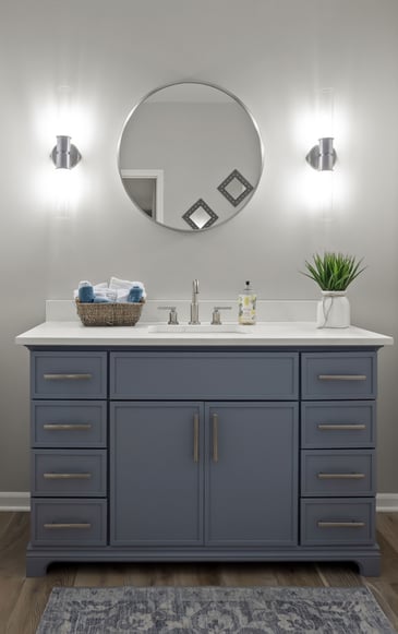 Bathroom with navy blue vanity, round mirror, brushed nickel hardware, and white quartz top accented by soft modern sconces.