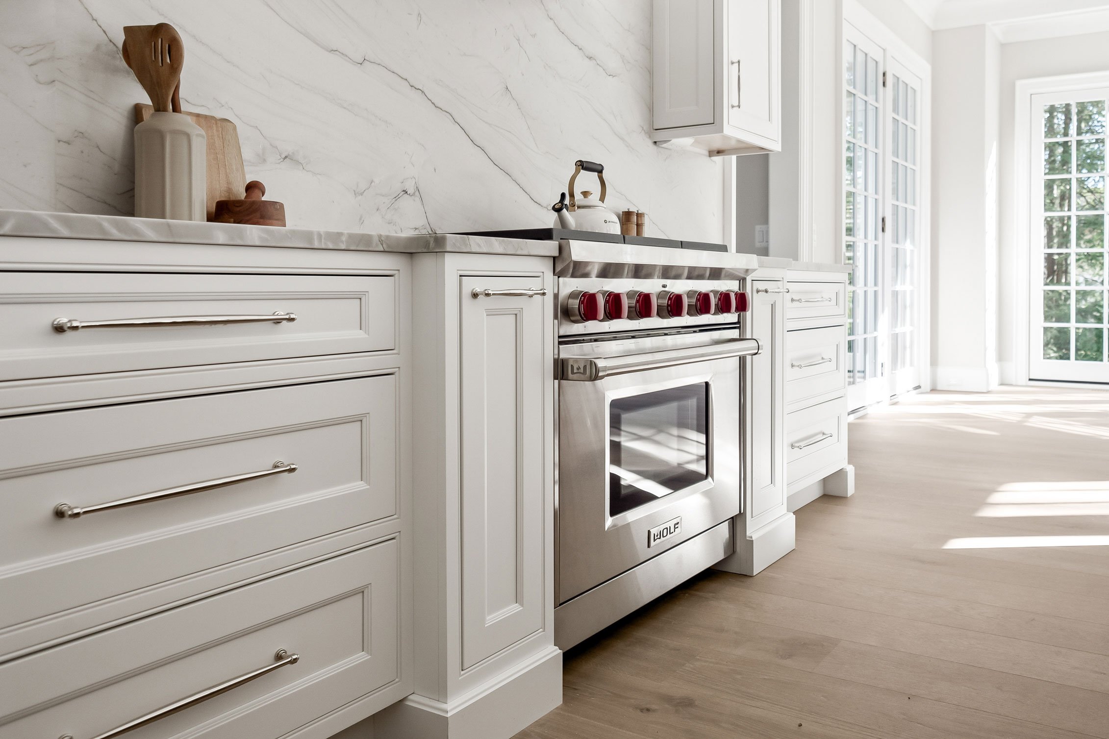 Cabinetry detail showing inset cabinetry in soft white flanking a Wolf range in a transitional kitchen.