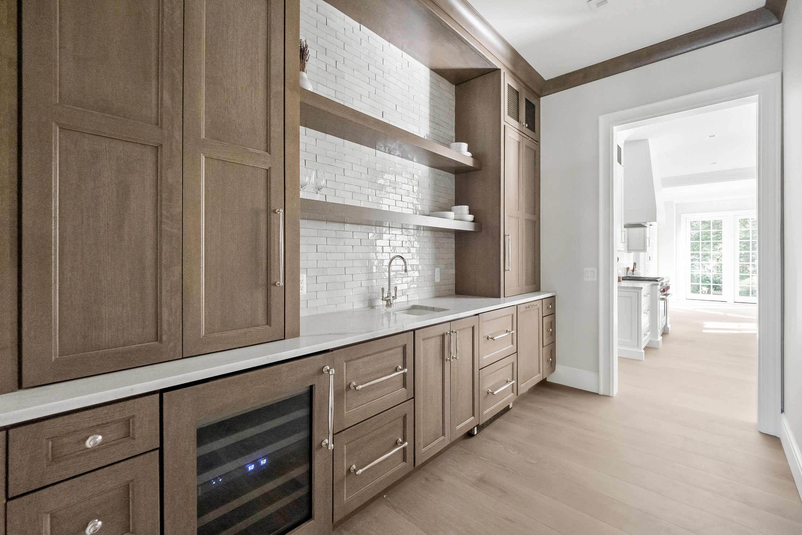 Butler’s pantry with warm wood cabinetry, open shelving, and wine refrigerator connecting kitchen and dining areas for effortless entertaining.