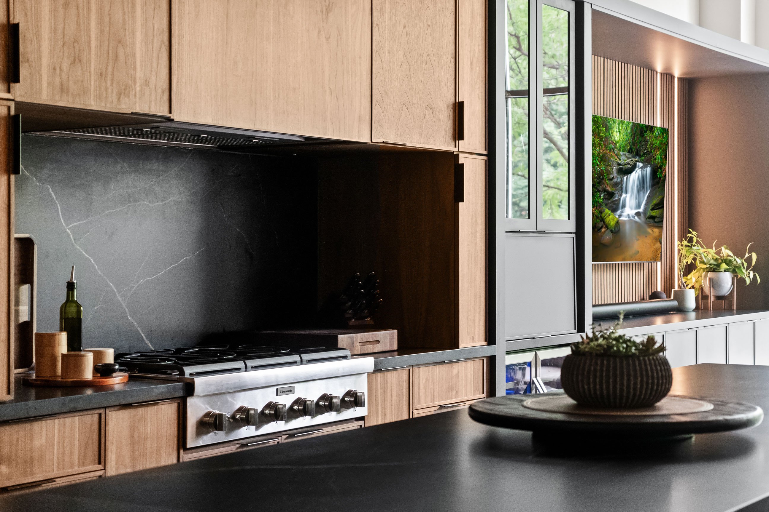 Large island with black countertop and walnut cabinetry on kitchen perimeter