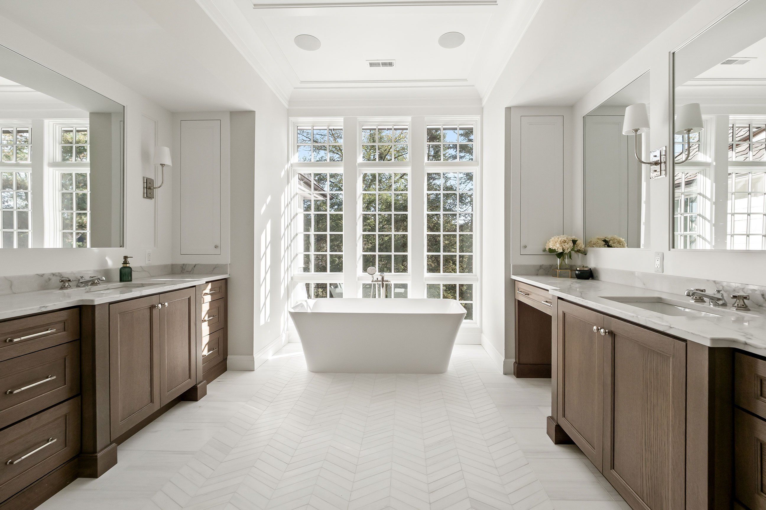 Primary bathroom with freestanding tub, natural light, and warm oak vanities designed by KSI for a serene, spa-like atmosphere.