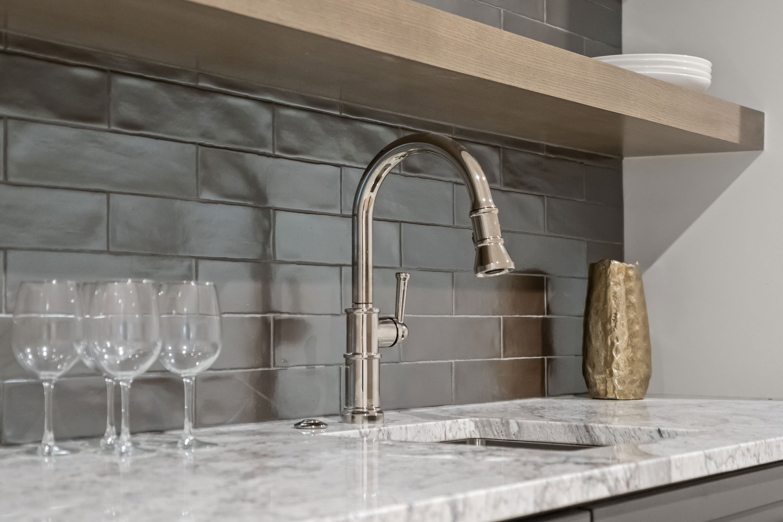 Sink detail in basement bar featuring floating shelves and gray tile backsplash.