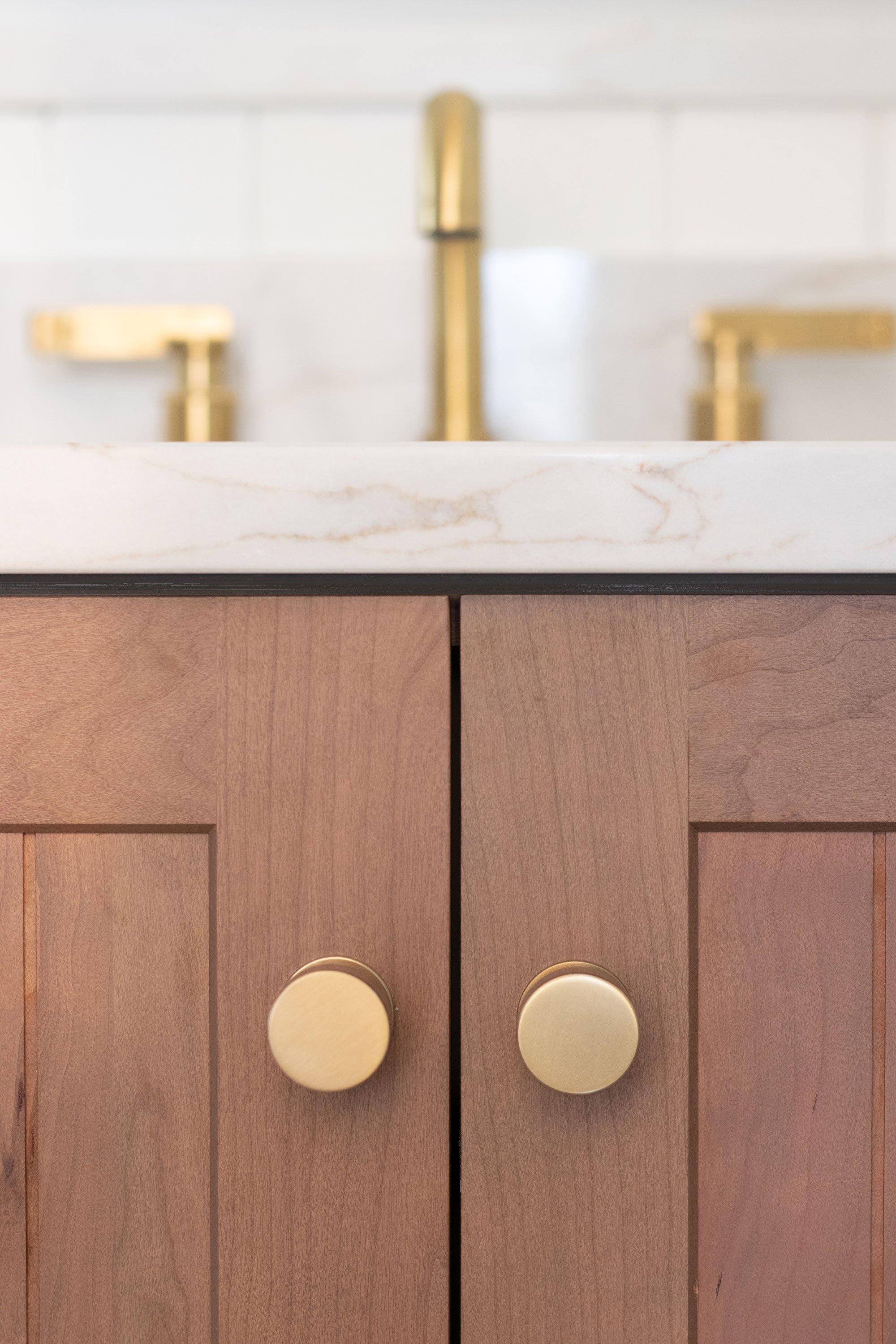 Detail of warm wood cabinetry with gold knobs and faucet