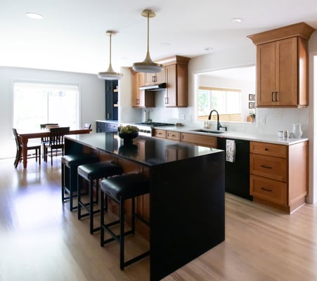 Warm kitchen remodel featuring shaker cabinetry with warm wood stain and black accents, with black quartz waterfall countertop on island - 3/4 view