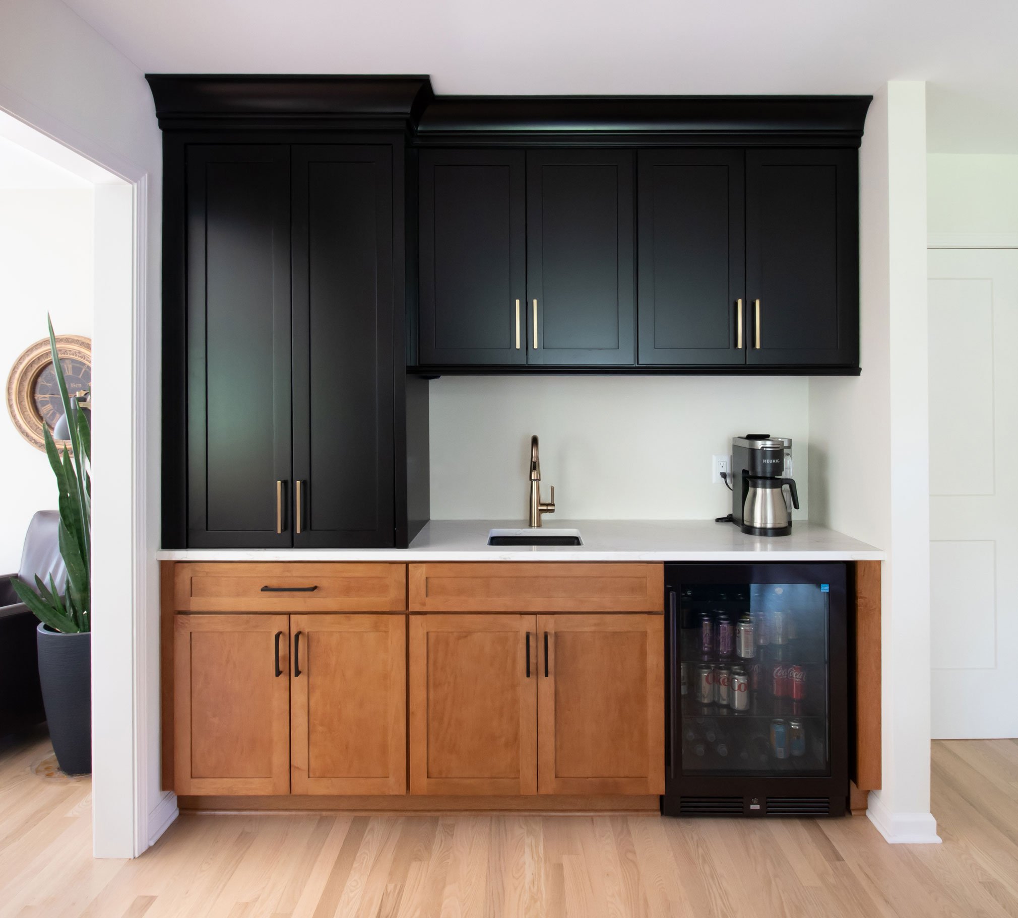 Beverage center featuring shaker cabinetry with warm wood stain and black accents, with pocket doors in left tower