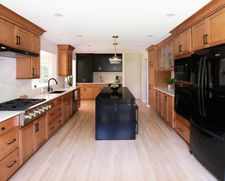 Warm kitchen remodel featuring shaker cabinetry with warm wood stain and black accents, with black quartz waterfall countertop on island - view from dining area