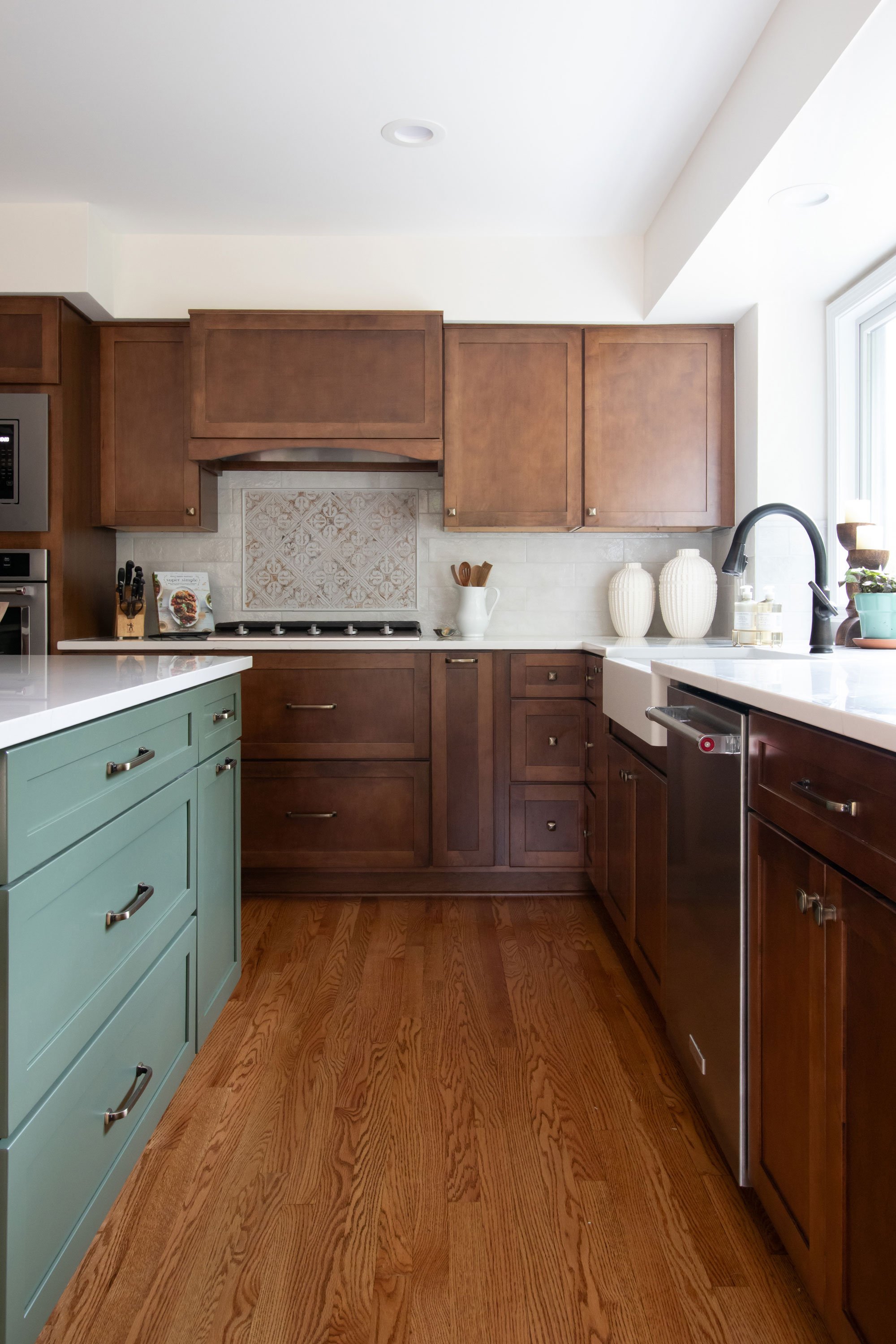 Remodeled kitchen with Merillat Masterpiece cabinetry in the Martel door style, featuring maple wood in Cognac finish on the perimeter and Evergreen paint on the island, and white quartz countertops.