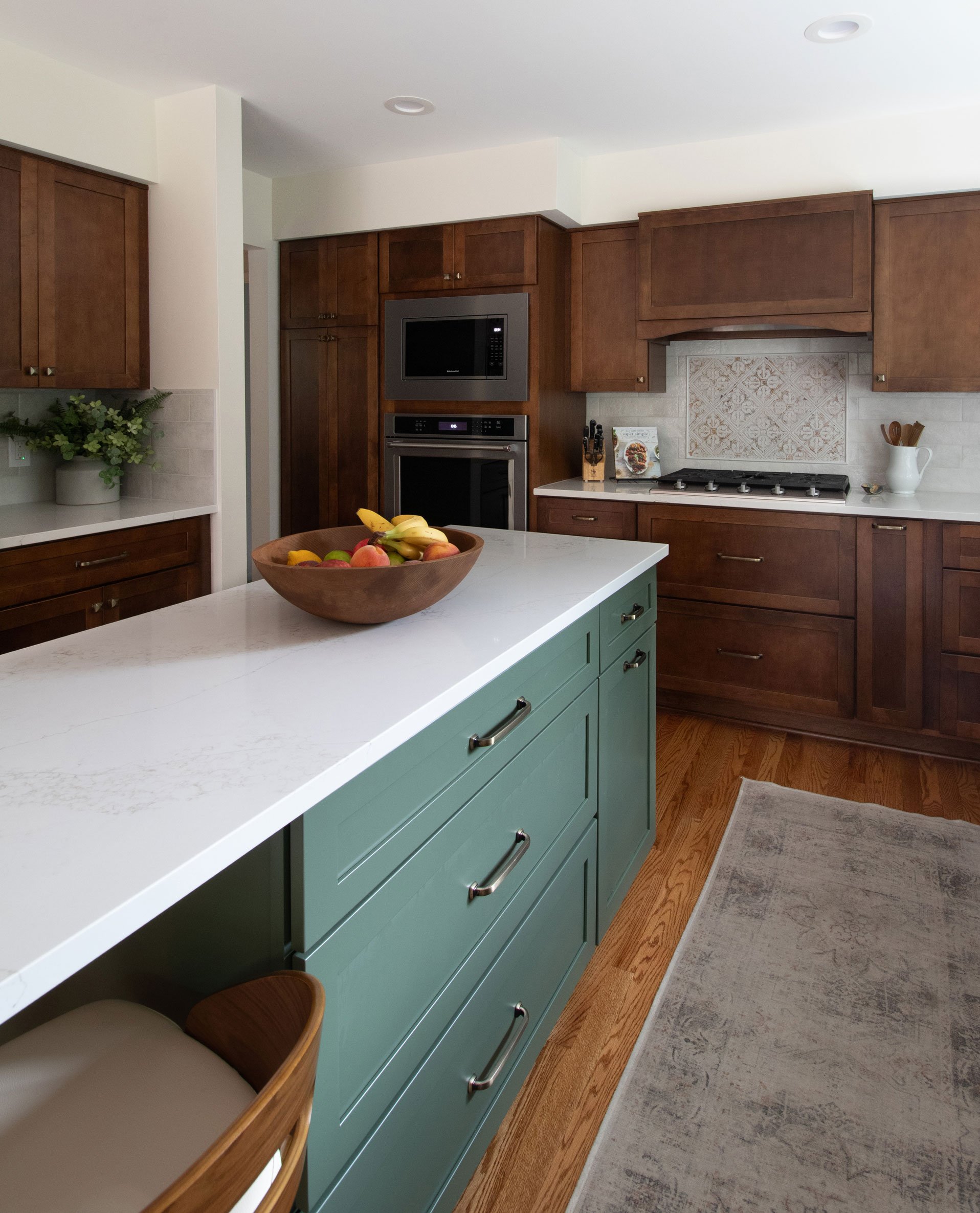 Green kitchen island featuring Merillat Masterpiece cabinetry in the Martel door style with Evergreen paint finish with white quartz countertop and seating for two.