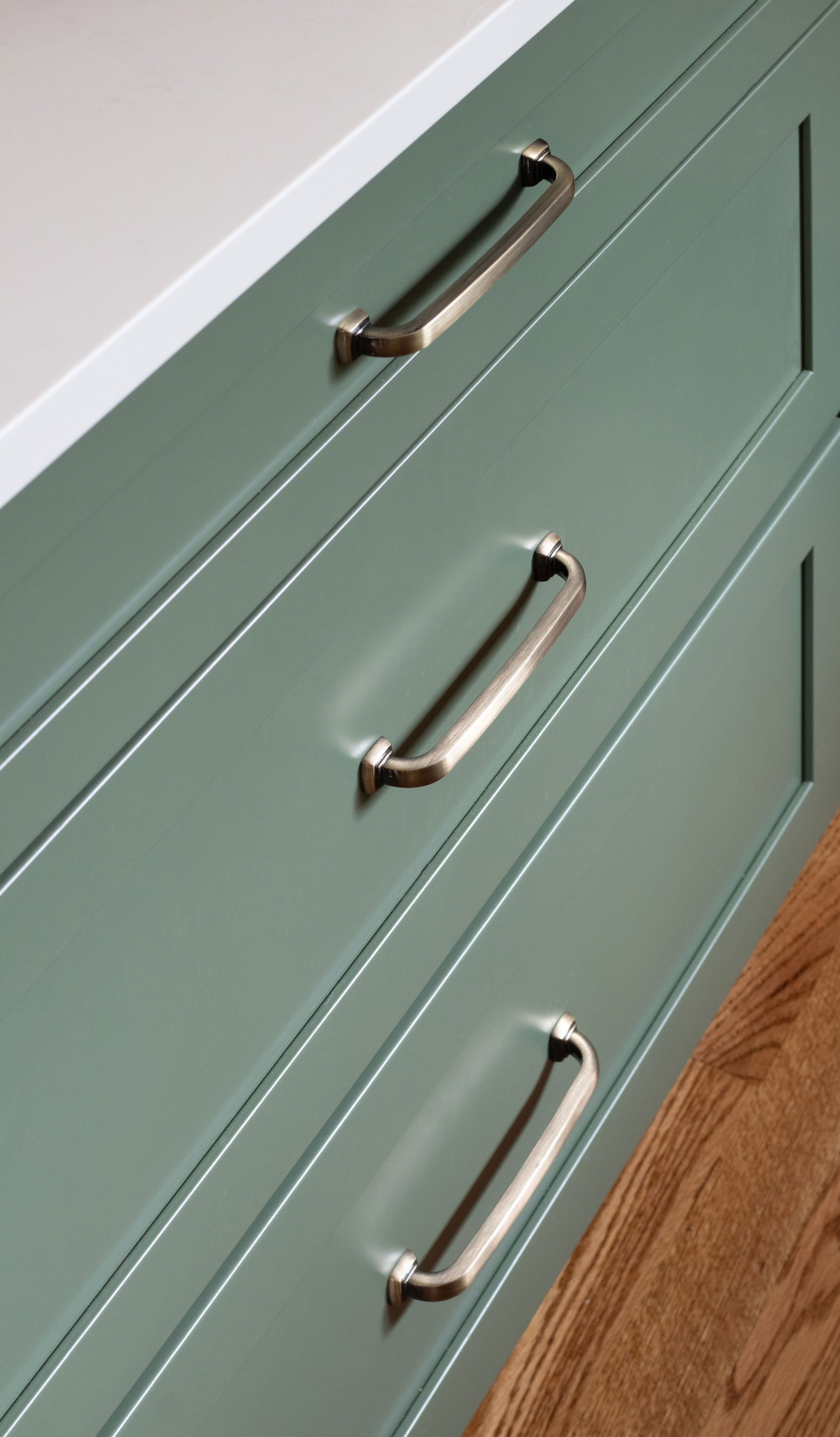 Green kitchen island featuring Merillat Masterpiece cabinetry in the Martel door style with Evergreen paint finish with white quartz countertop.