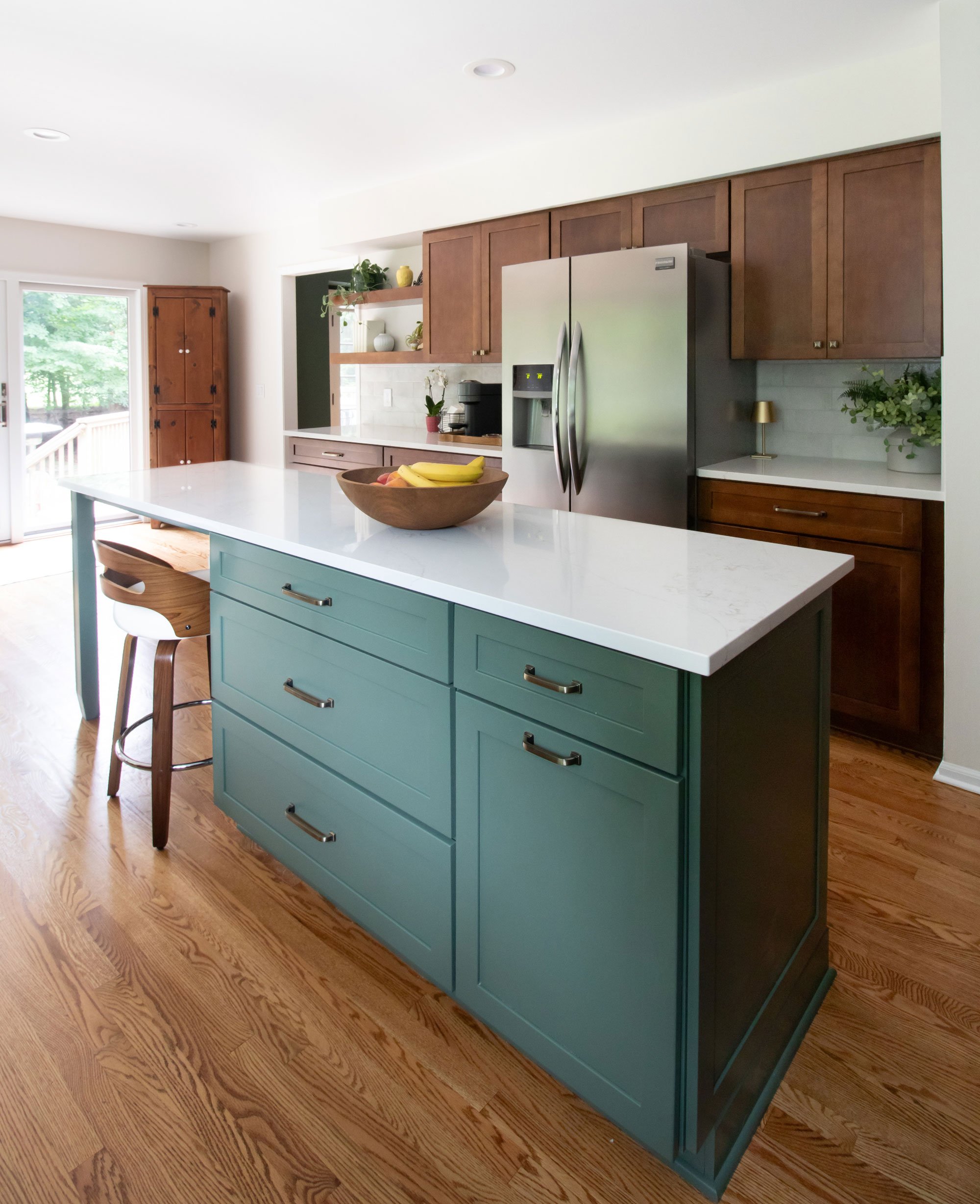 Green kitchen island featuring Merillat Masterpiece cabinetry in the Martel door style with Evergreen paint finish with white quartz countertop and seating for two.