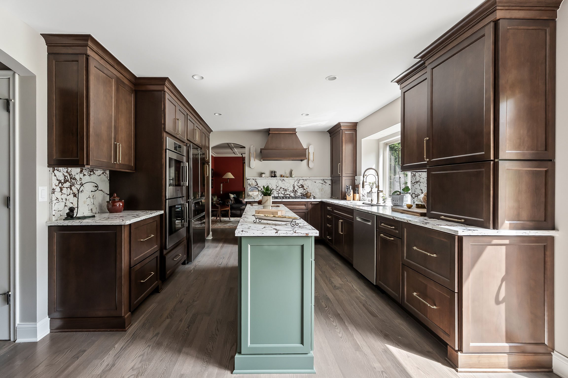 A dramatic, layered kitchen remodel in Rochester Hills featuring rich Brown Sugar cherry cabinetry, a sage green island, and a full-height veined stone backsplash.