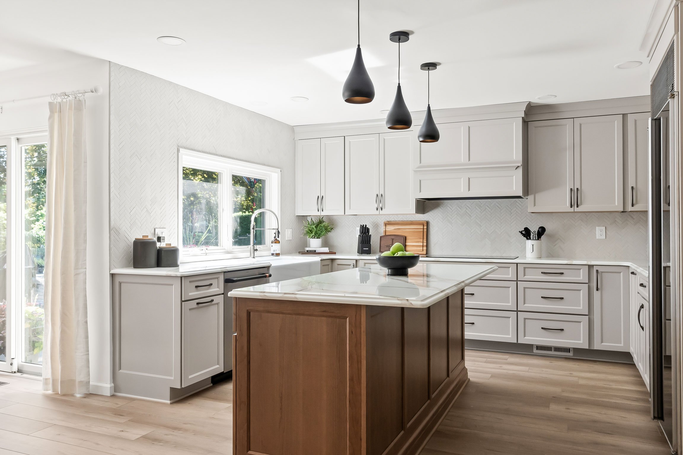 The kitchen's window wall and sliding glass door, showing the herringbone tile accent wall, greige cabinetry, and wood-toned island.