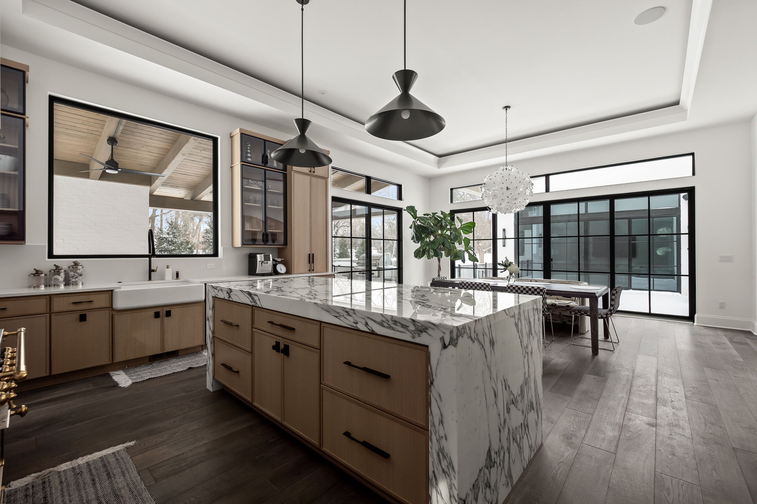 View from kitchen toward dining area showing generous island, wood-tone cabinetry, expansive windows, and open floor plan.