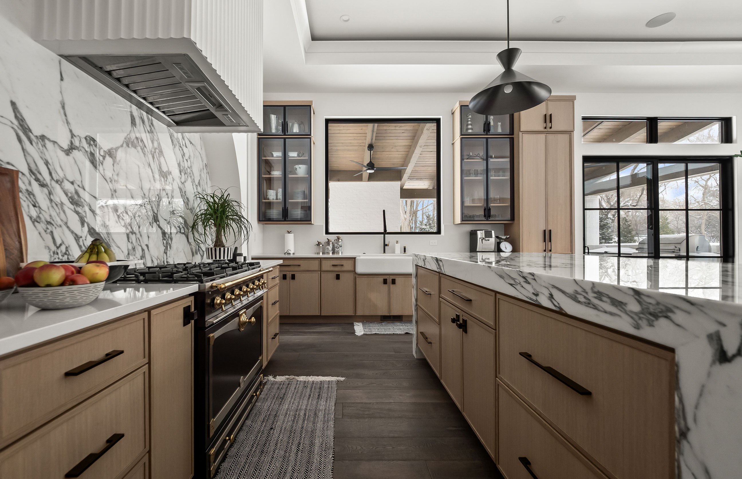 Stove and countertop area with marble backsplash, black range, farmhouse sink, and warm wood cabinetry.