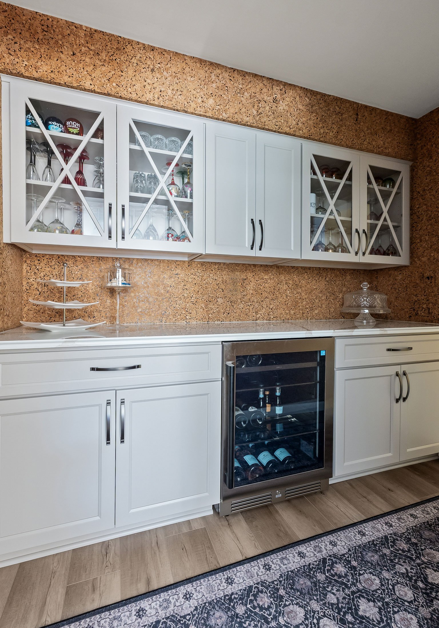 The butler's pantry bar area, featuring glass-front cabinets for glassware display, a built-in wine refrigerator, and the original cork wallpaper wall.