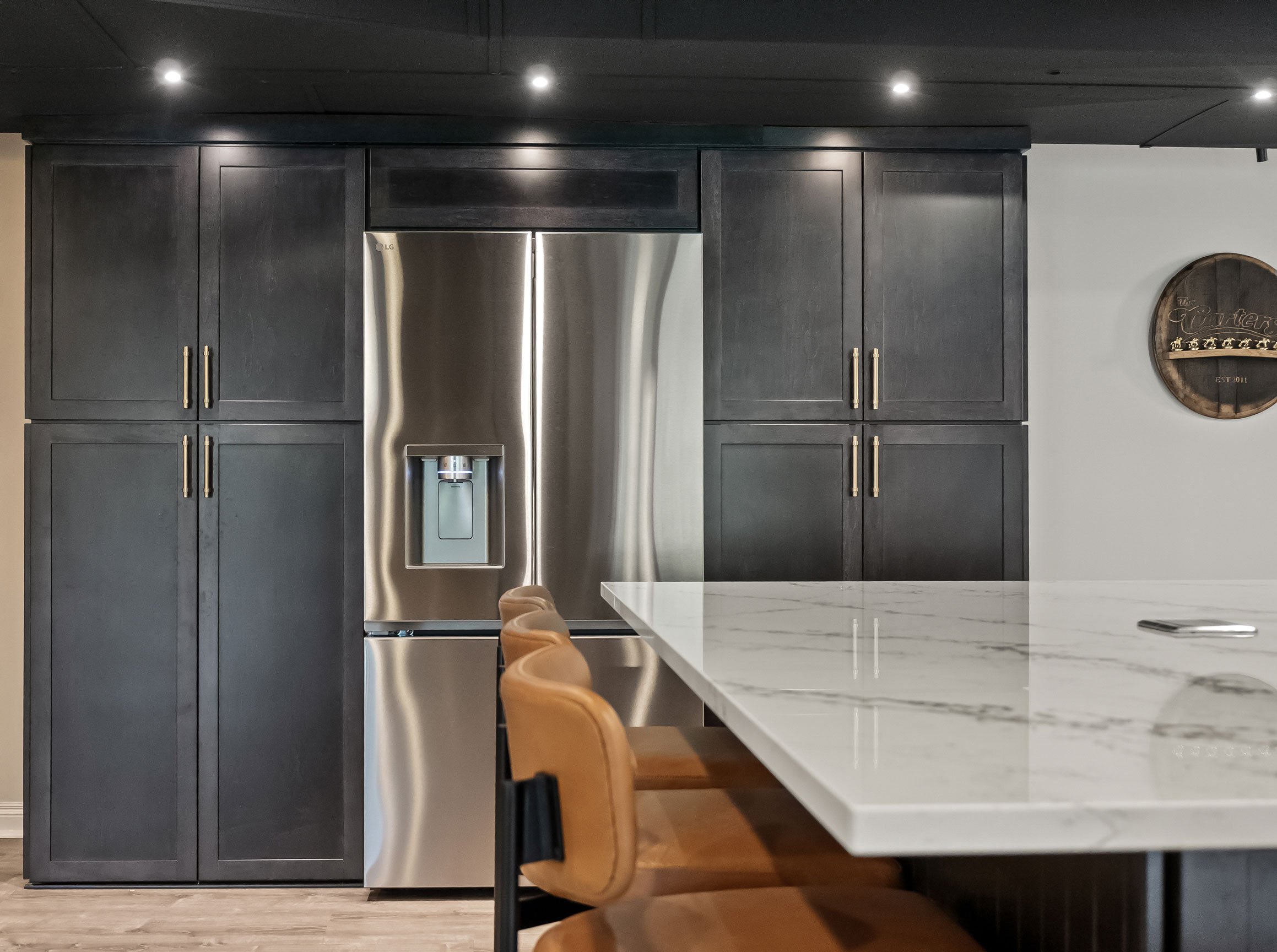 Basement kitchen with pantry, refrigerator, and kitchen island in foreground with ample seating.