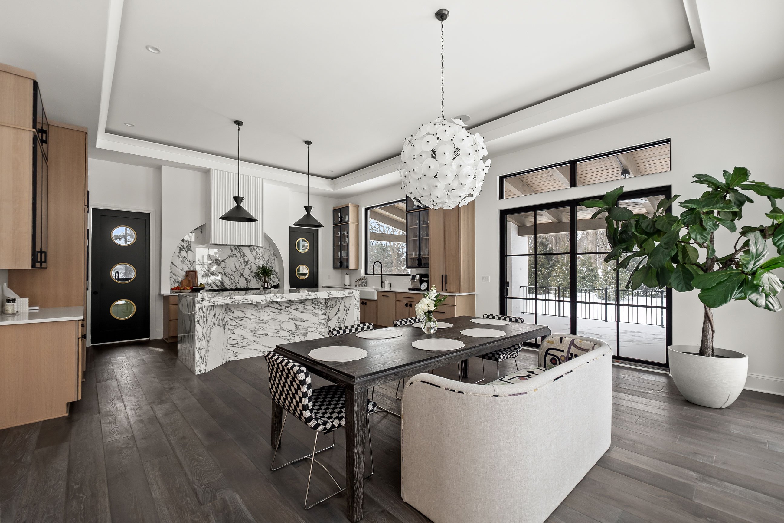 Modern kitchen with large quartersawn white oak cabinets, waterfall island with dramatic veined countertop, black metal pendant lights and mixed metal accents.