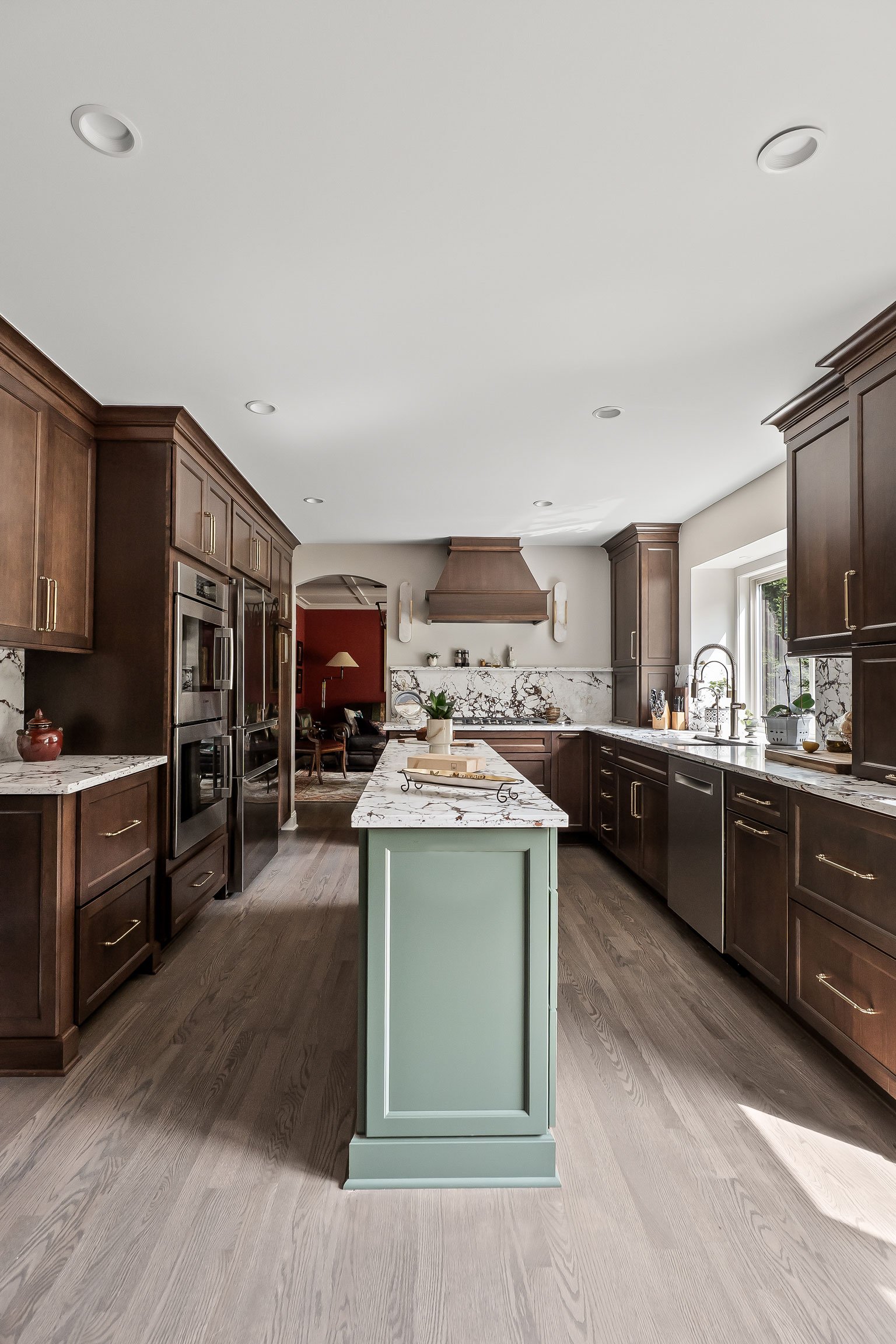 A sweeping view down the kitchen from the sink wall toward the range, showing the green island and cherry cabinetry throughout.