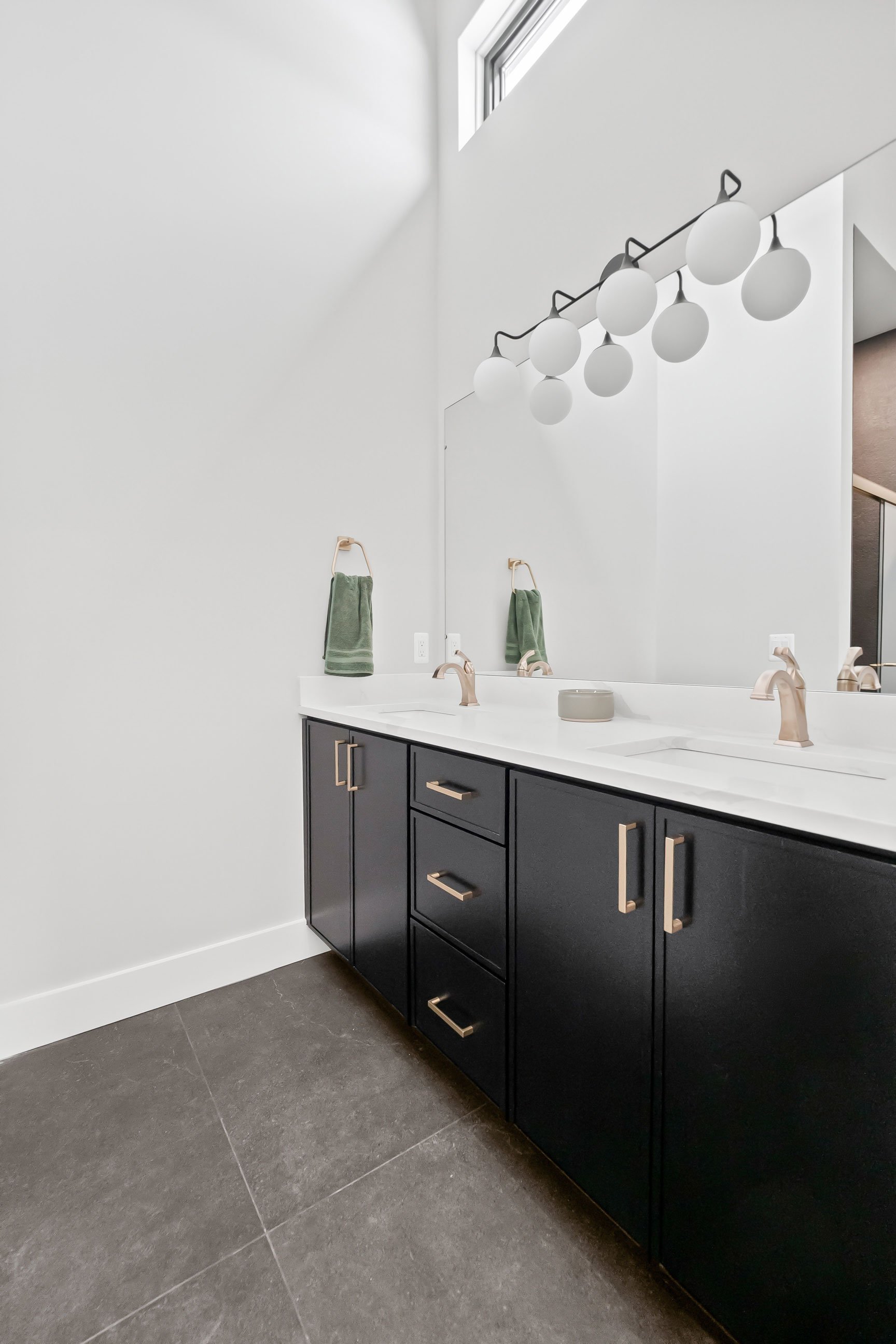 Dark moody bathroom vanity with black cabinetry, gold hardware, double sinks, and tall ceilings in barndominium home