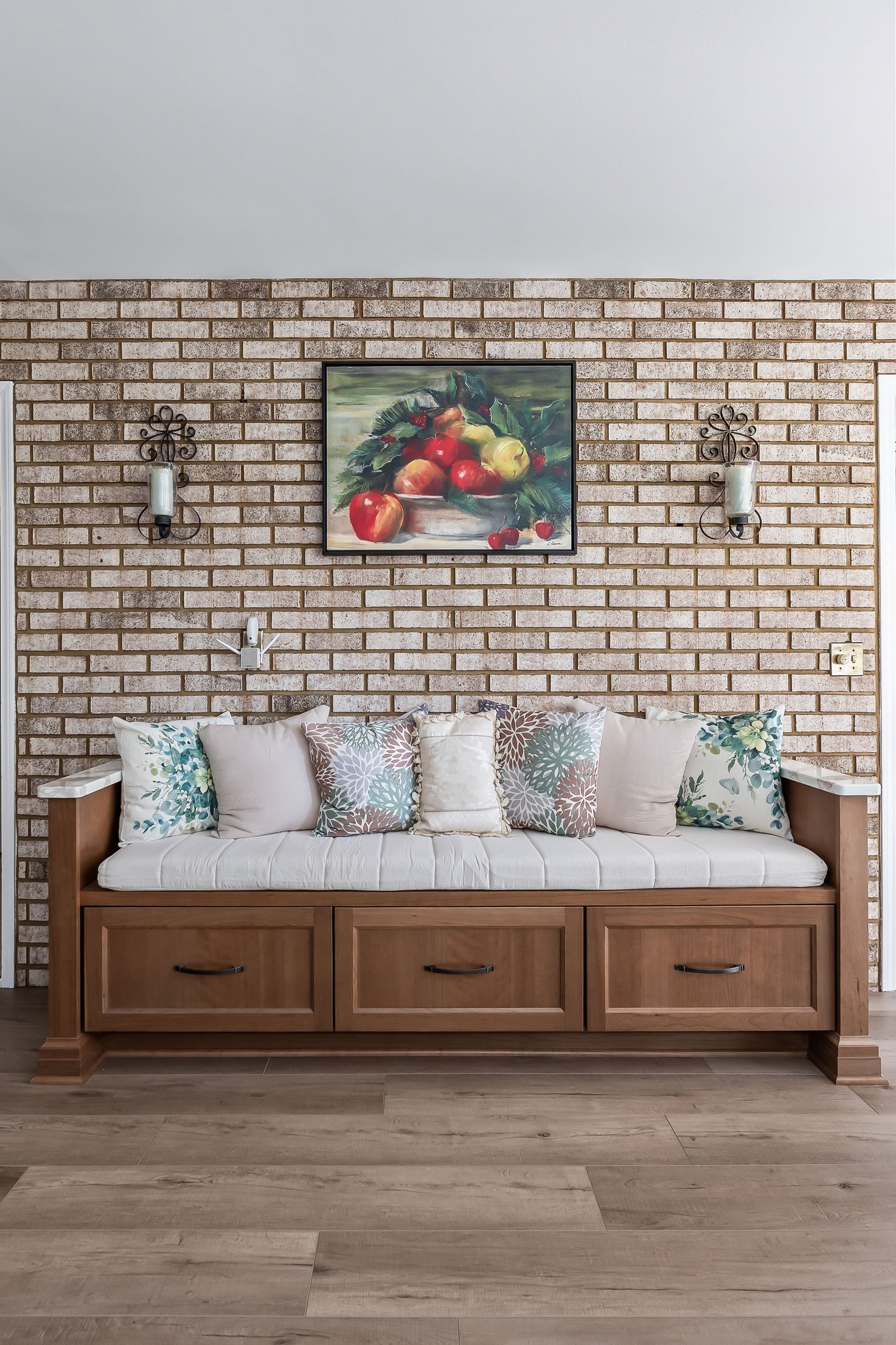 A built-in storage bench with a cushioned seat and decorative pillows, set against the home's original brick accent wall.