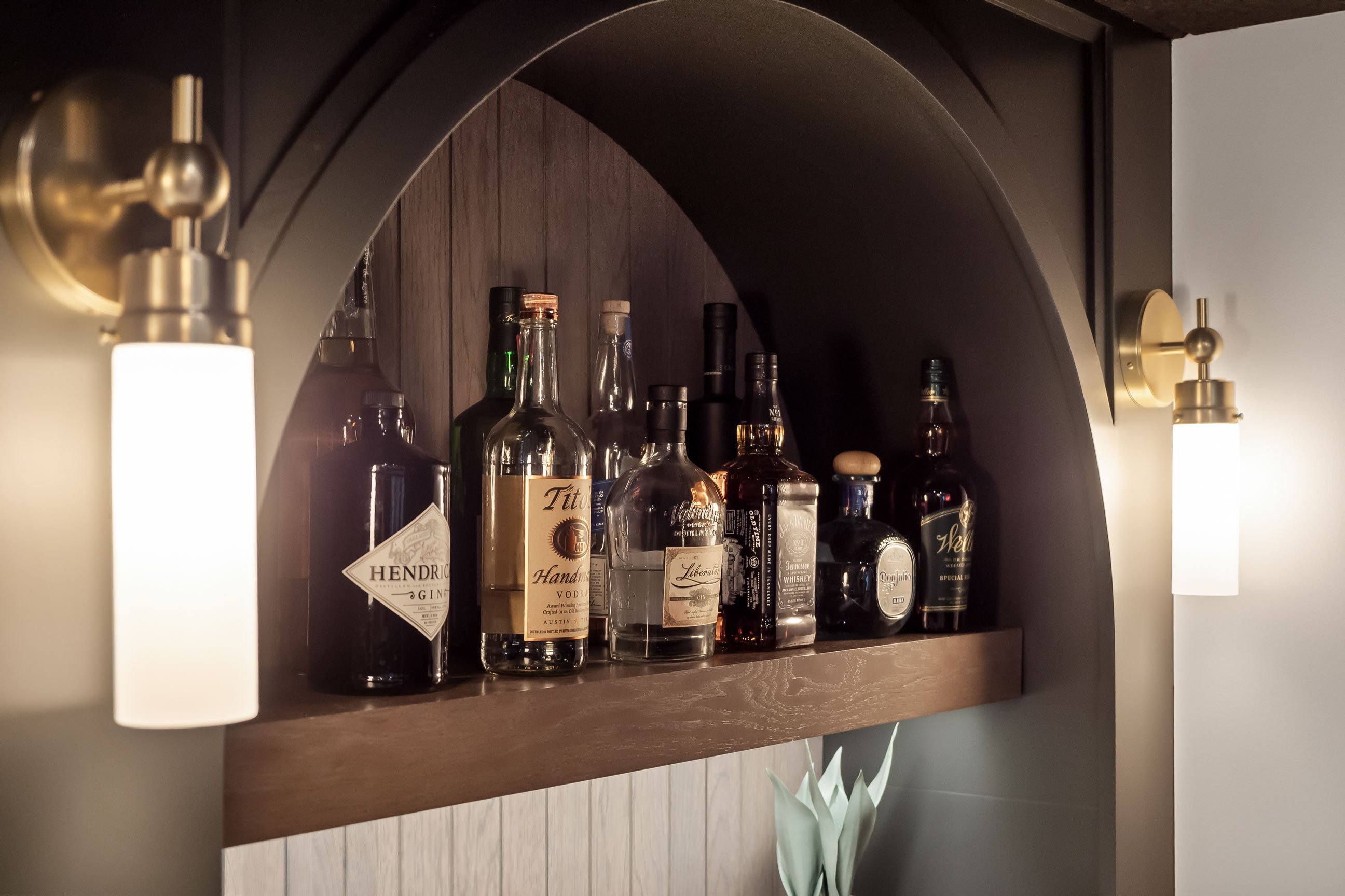Speakeasy-style basement bar detail with arches, floating wood shelves, and warm accent lighting.