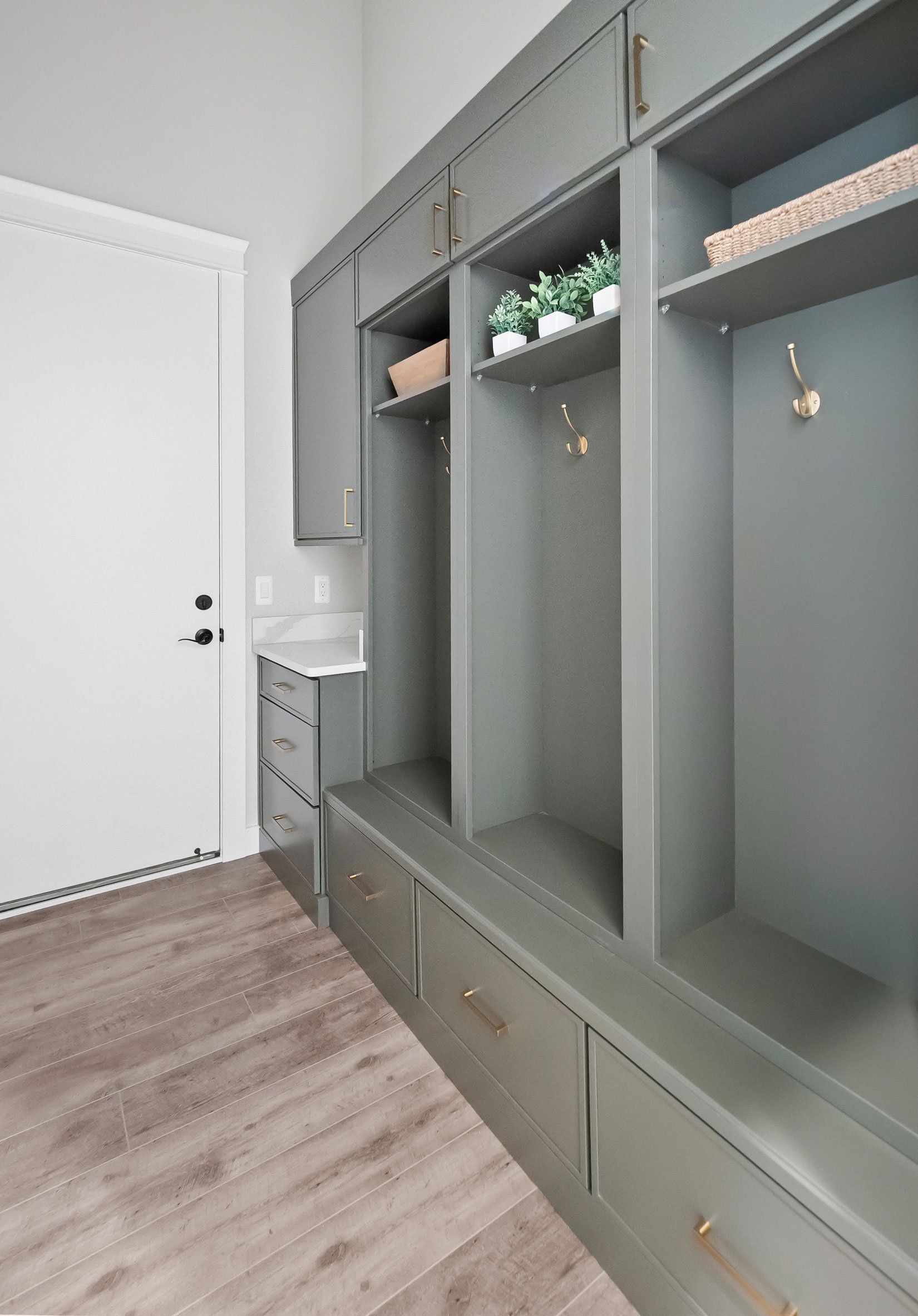 Custom mudroom cabinetry in soft green with built-in bench, storage cubbies, and gold hooks in modern barndominium